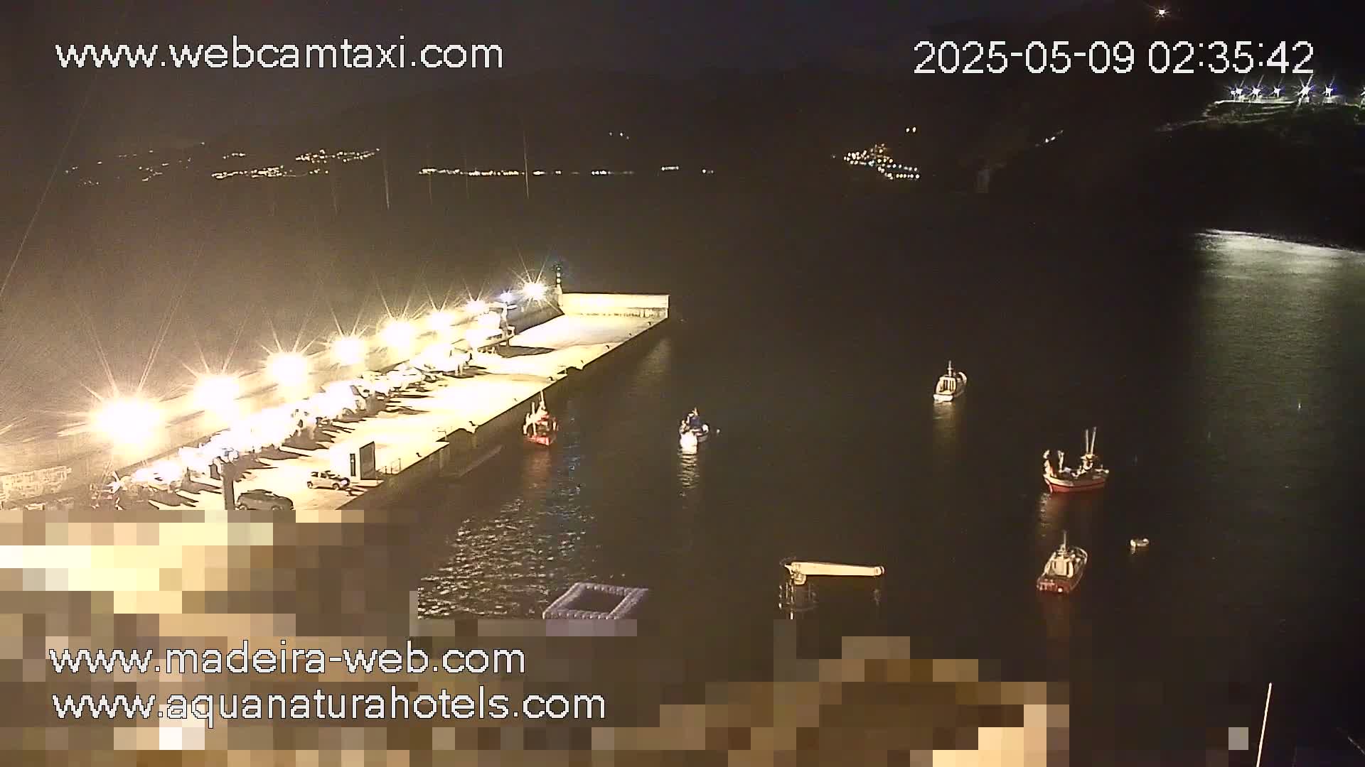 A brightly lit pier at night, with several small boats in the dark water surrounding it.