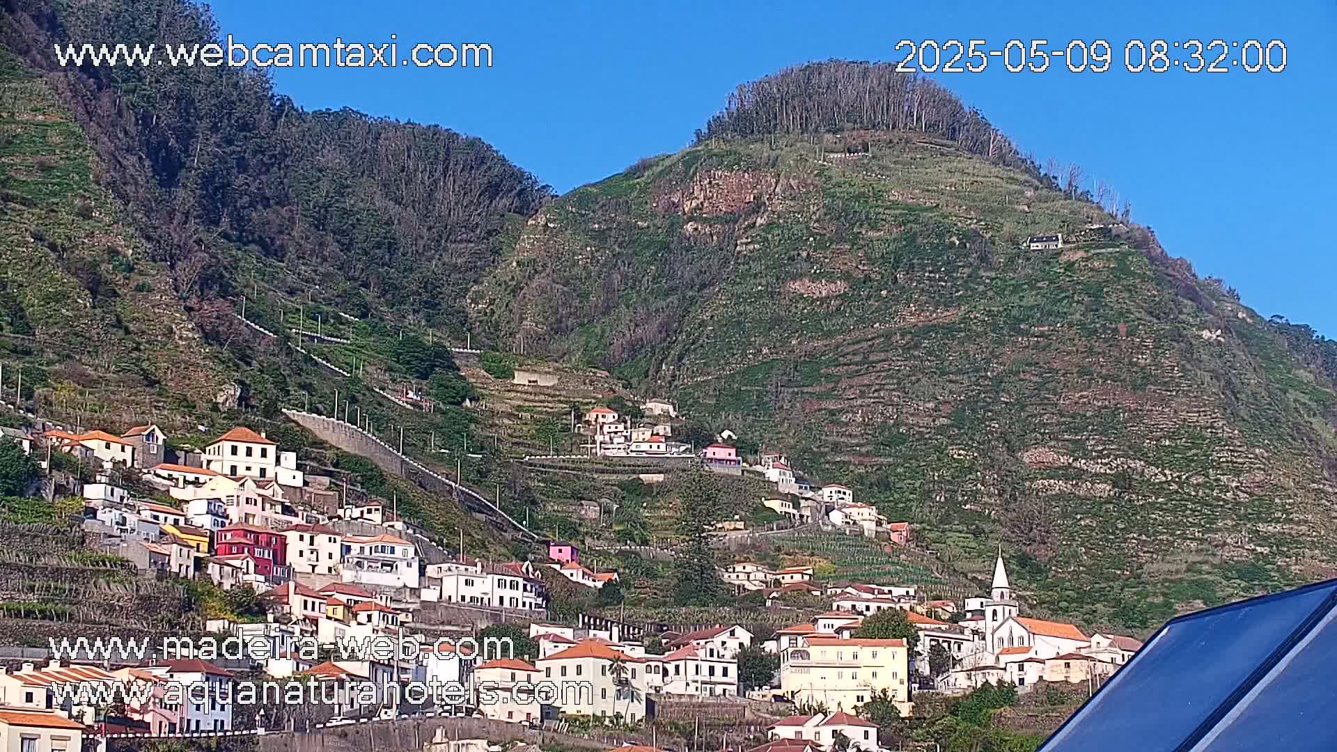 A hillside village clings to a terraced mountainside under a clear blue sky.