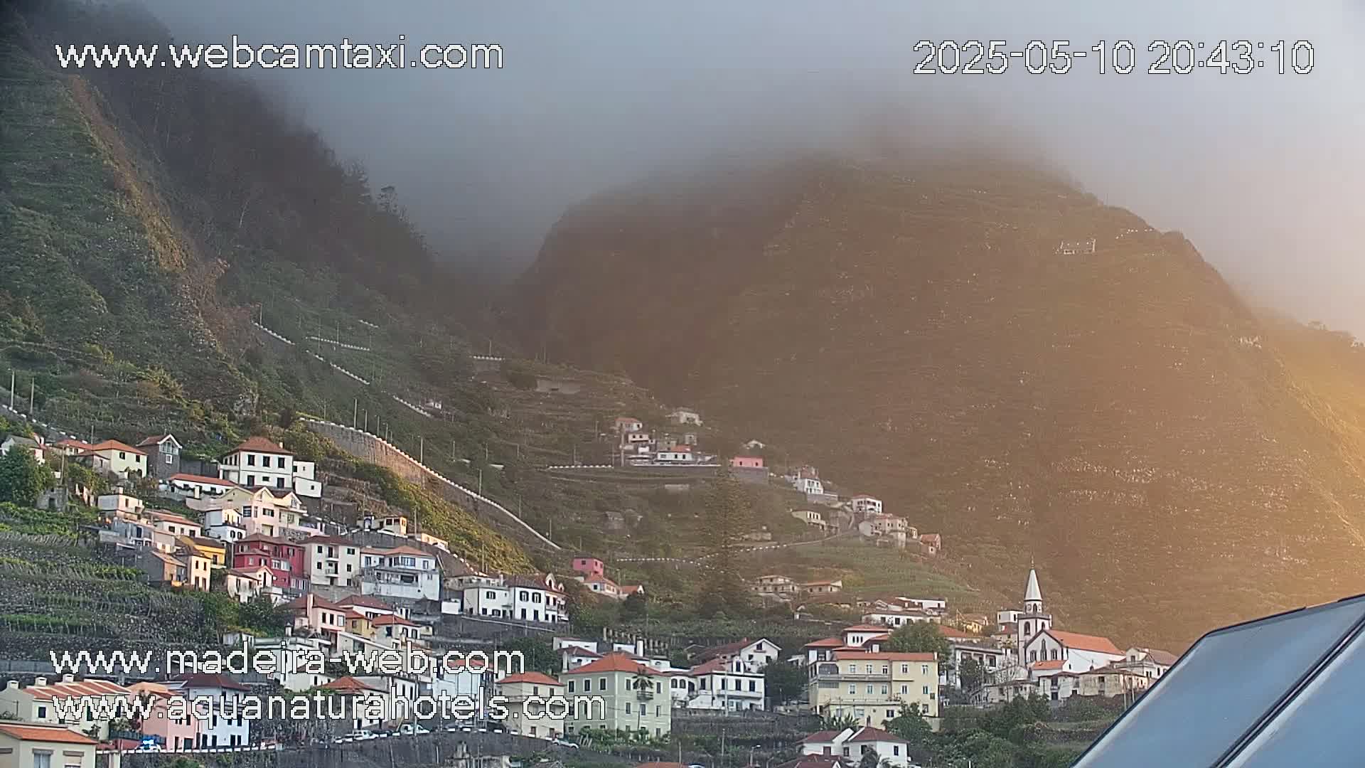 A hillside village clings to a steep, fog-shrouded mountainside at sunset.