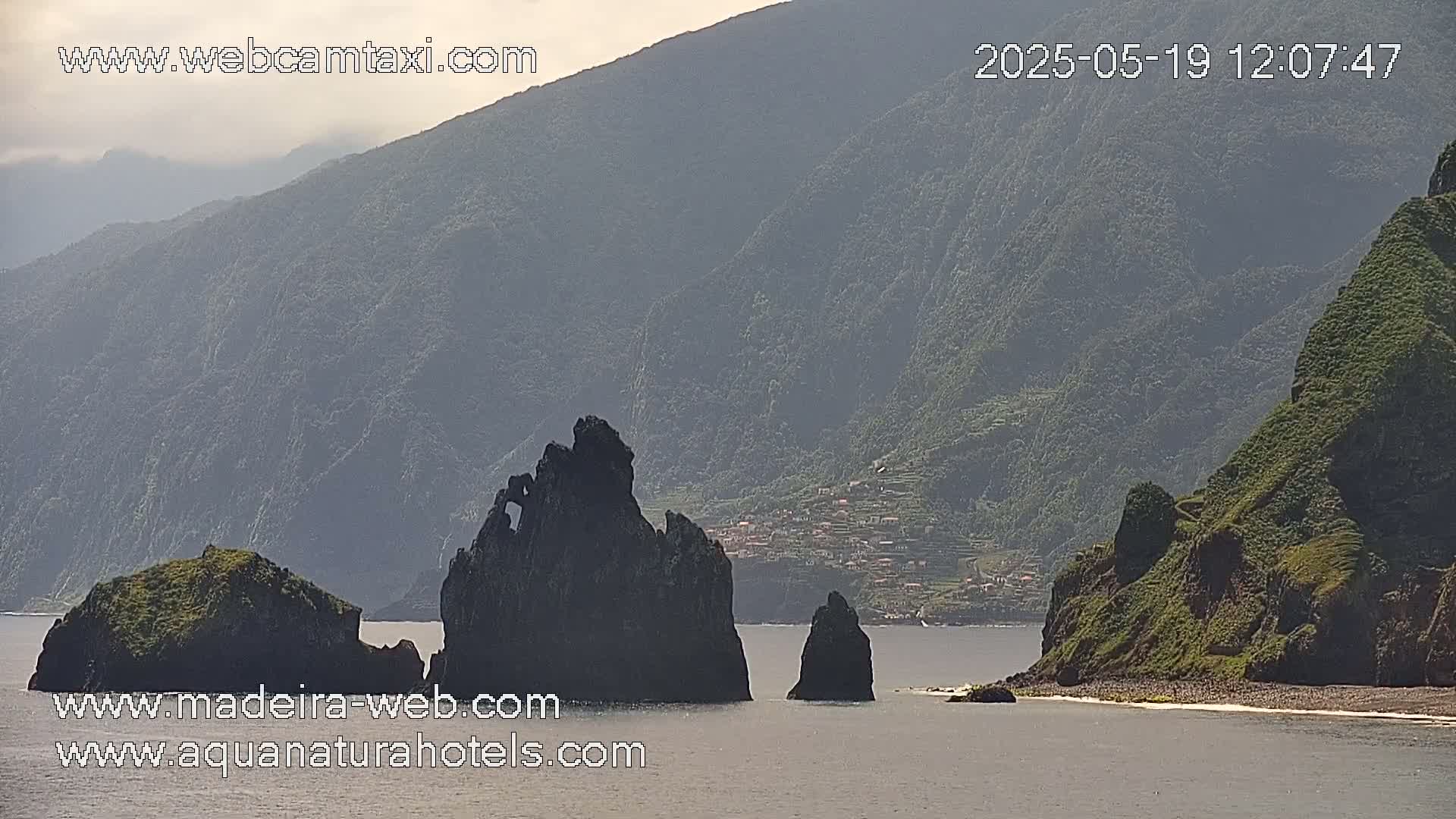 A hazy view shows dark, rocky islets and a mountainous coastline under a partly cloudy sky.