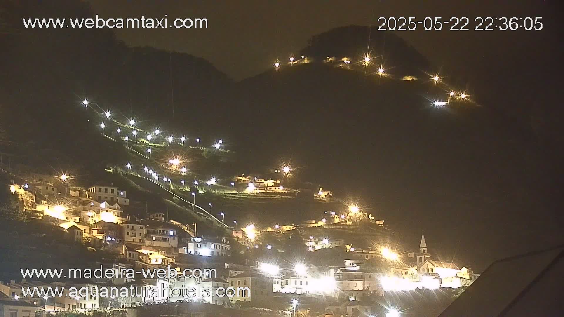 A hillside village is illuminated at night by many streetlights, showing numerous buildings nestled into the mountainside.