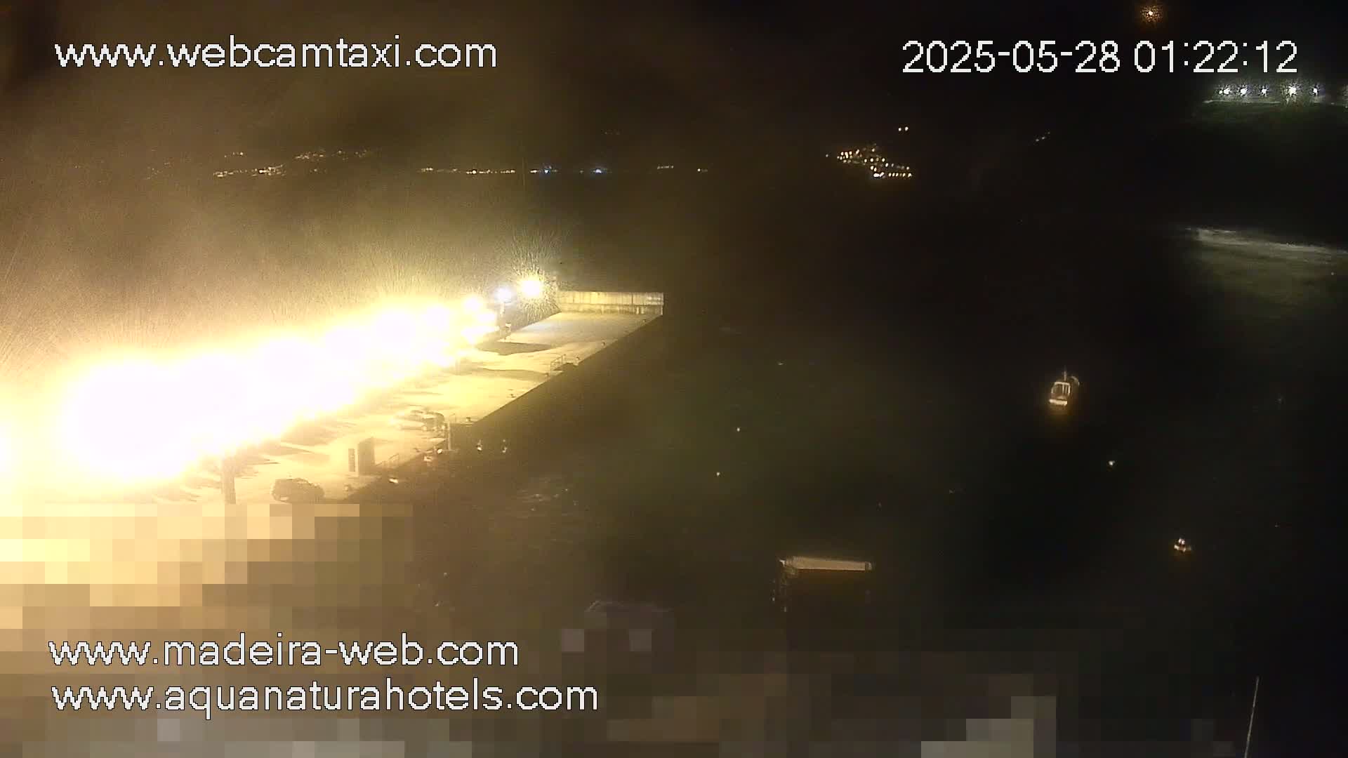 A nighttime, brightly lit waterfront area is seen with a boat in the water and heavy spray or mist obscuring visibility.