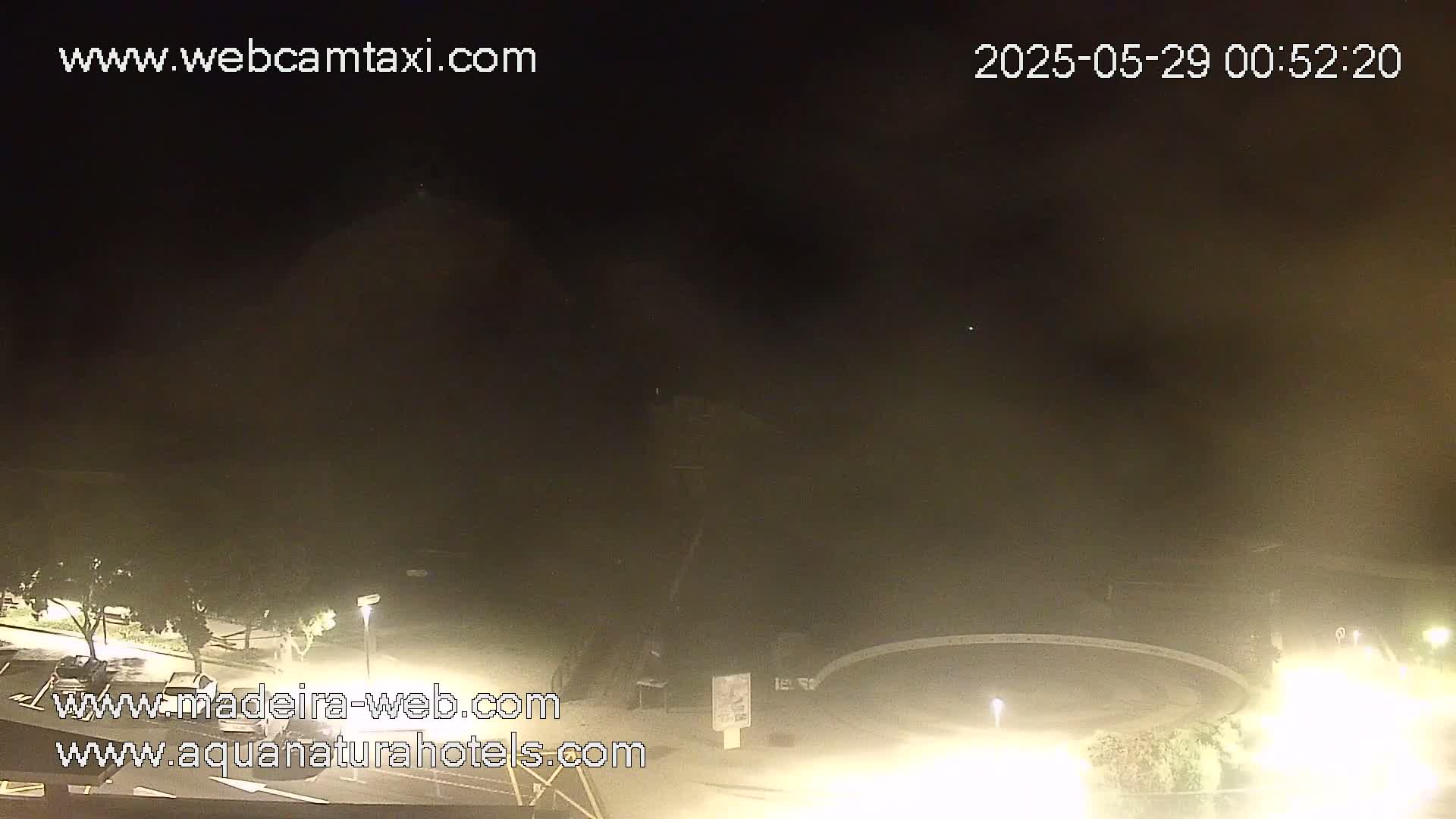 A nighttime, hazy view of a parking lot and a dimly lit, circular area, possibly a pool, with some vegetation visible.