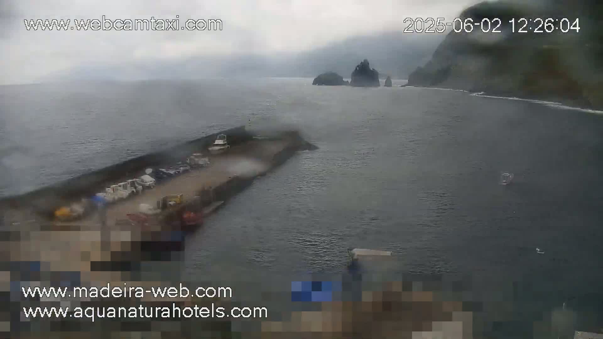 A hazy, overcast day reveals a harbor with several boats docked near a rocky coastline.