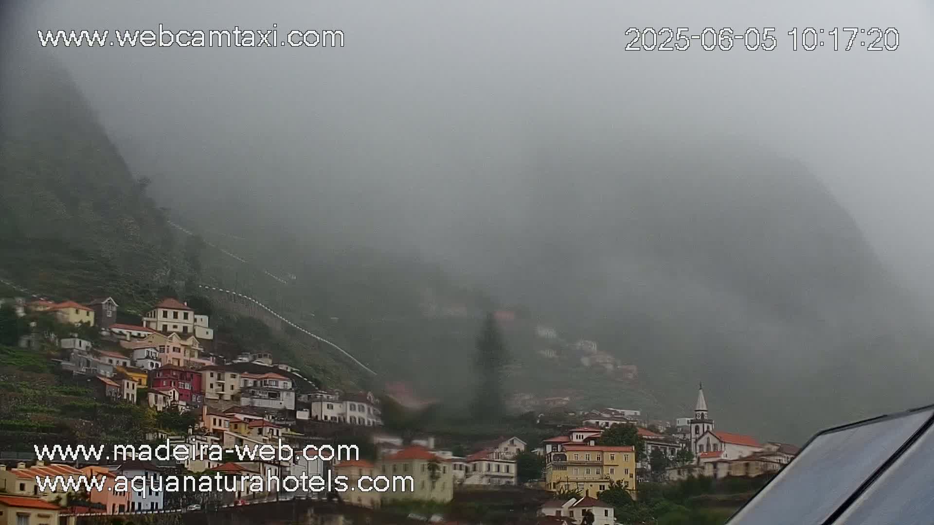 A foggy hillside village with colorful buildings and a church steeple is visible through a thick fog.