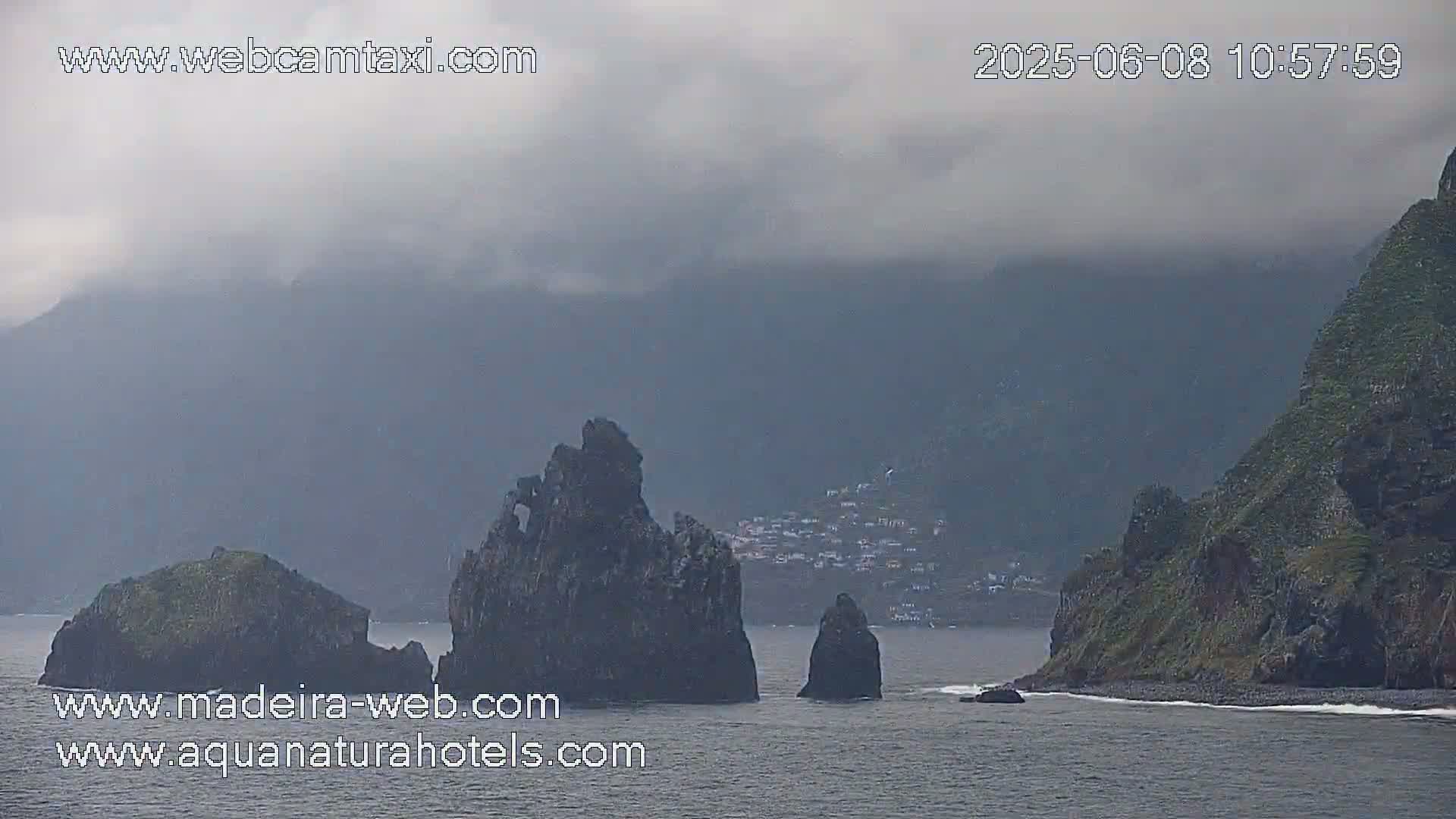 A cloudy day shows rocky outcroppings and a small village nestled in a mountainous coastal area.