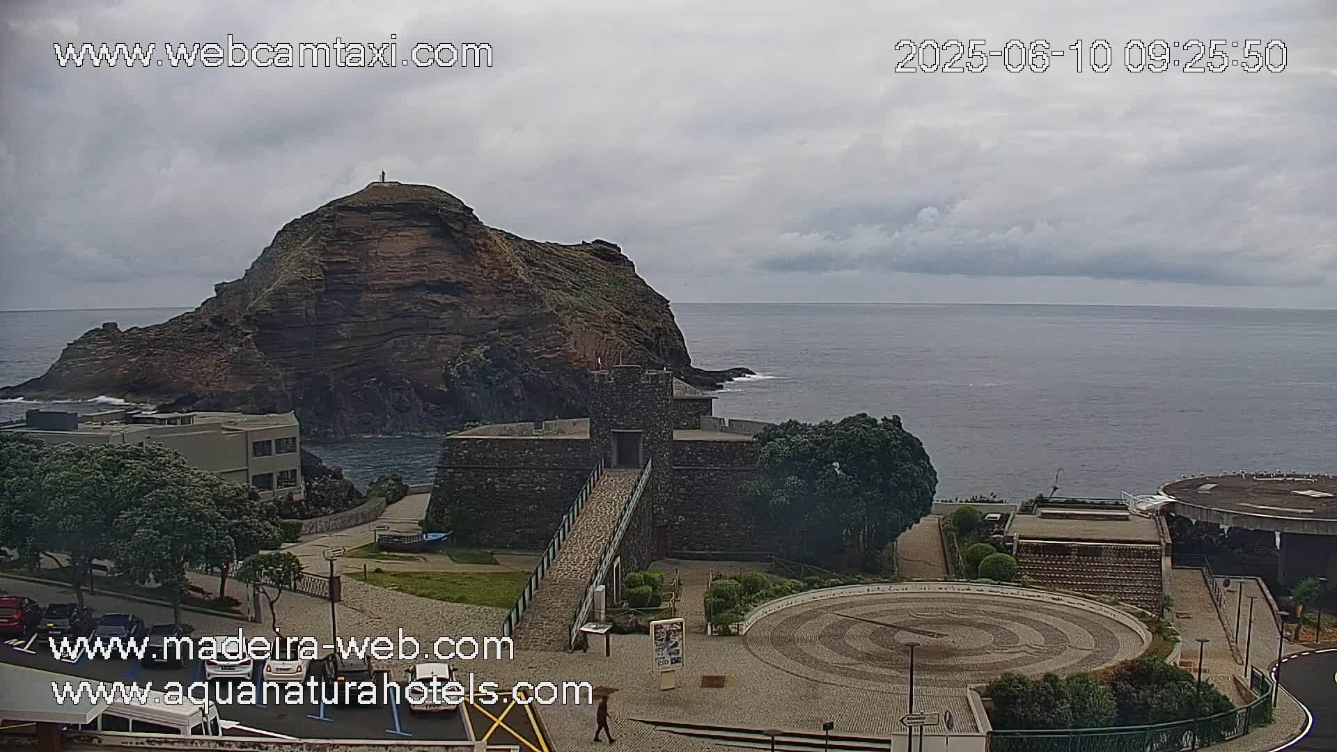 A stone structure and a rocky island are visible near the ocean under an overcast sky.