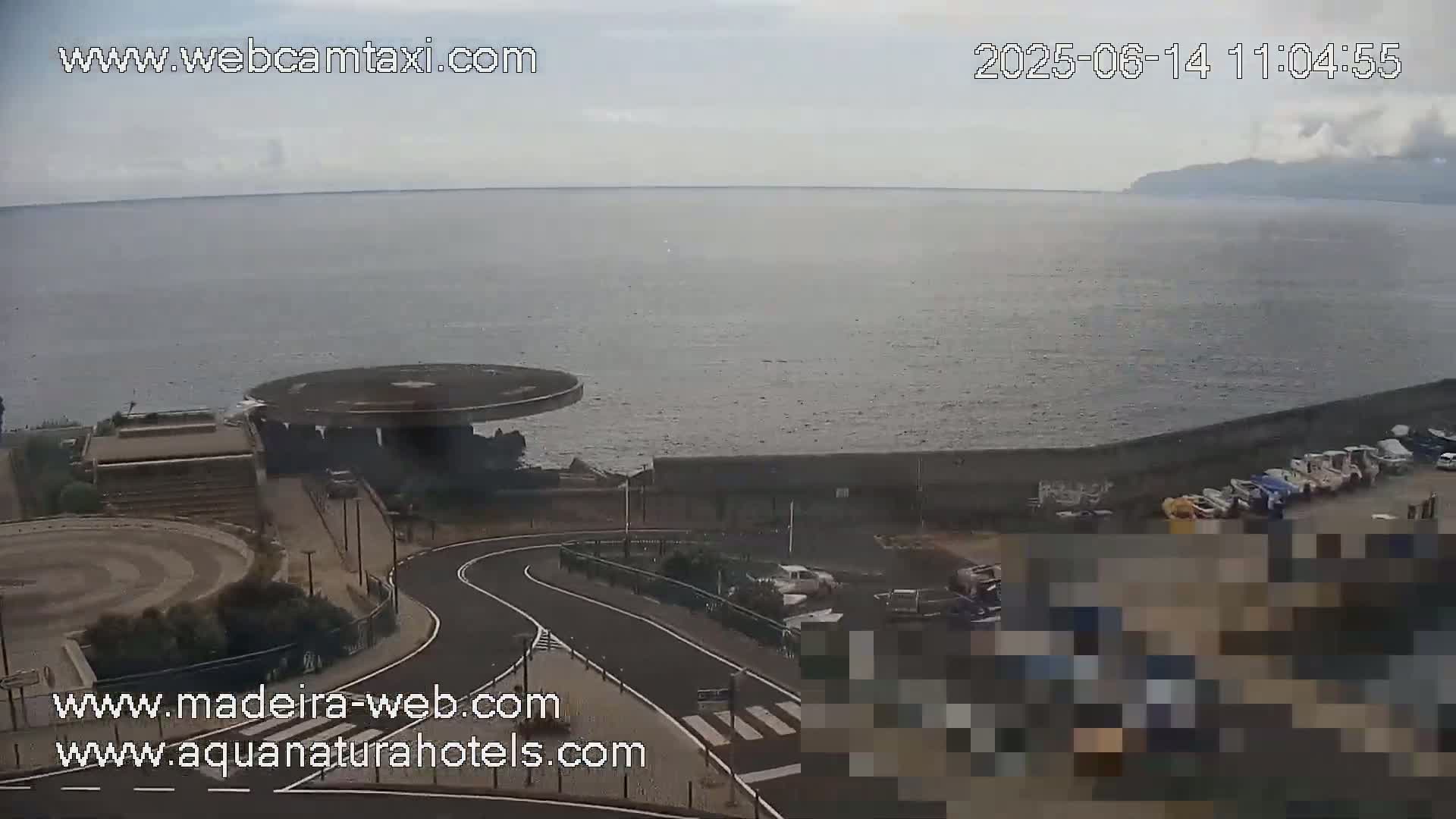 A coastal overlook shows a calm ocean under an overcast sky, with a curved roadway leading to a parking lot near a circular structure.