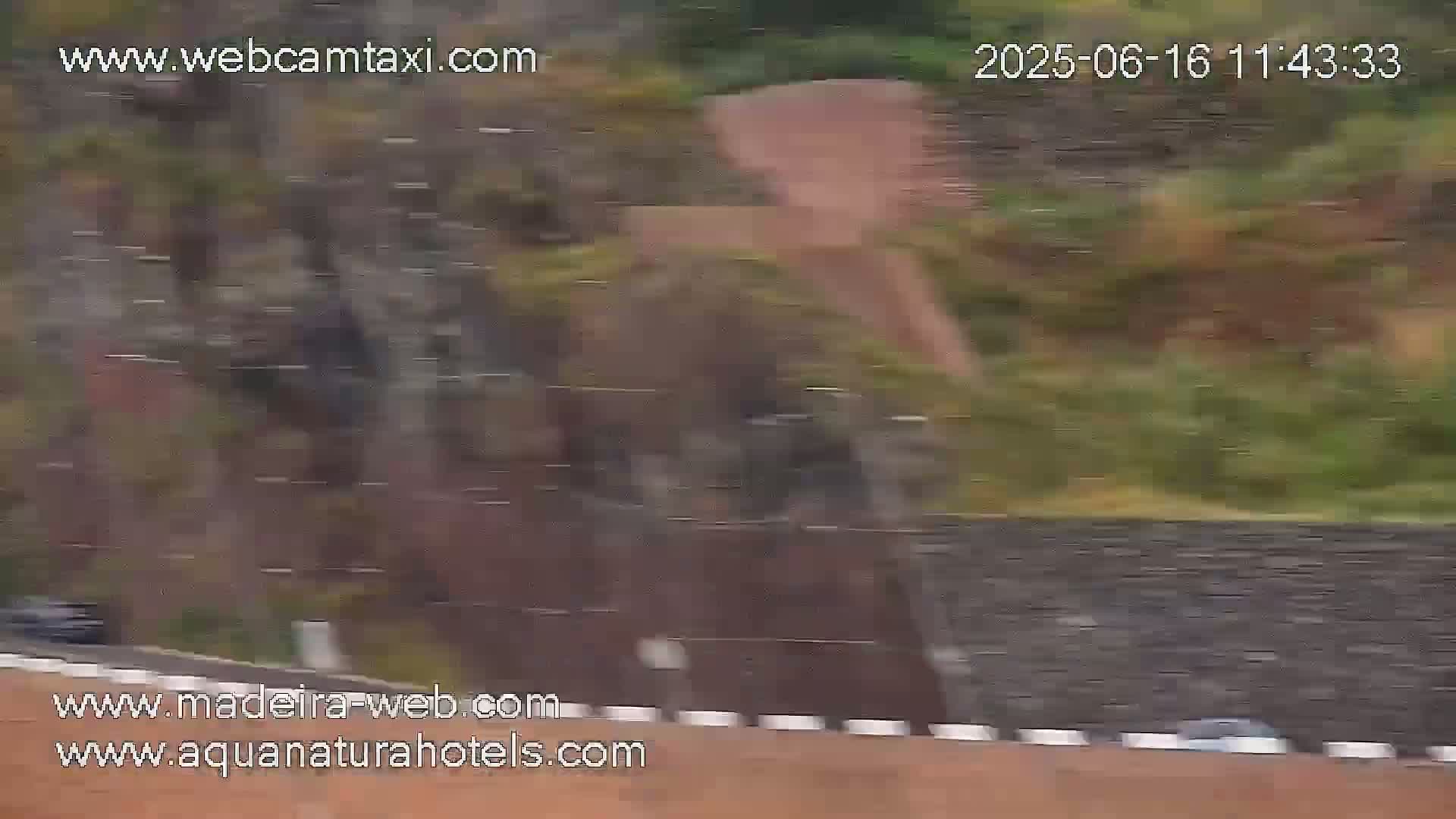 A blurry image shows a rain-swept roadway next to a stone wall and a hillside, possibly in a mountainous region.