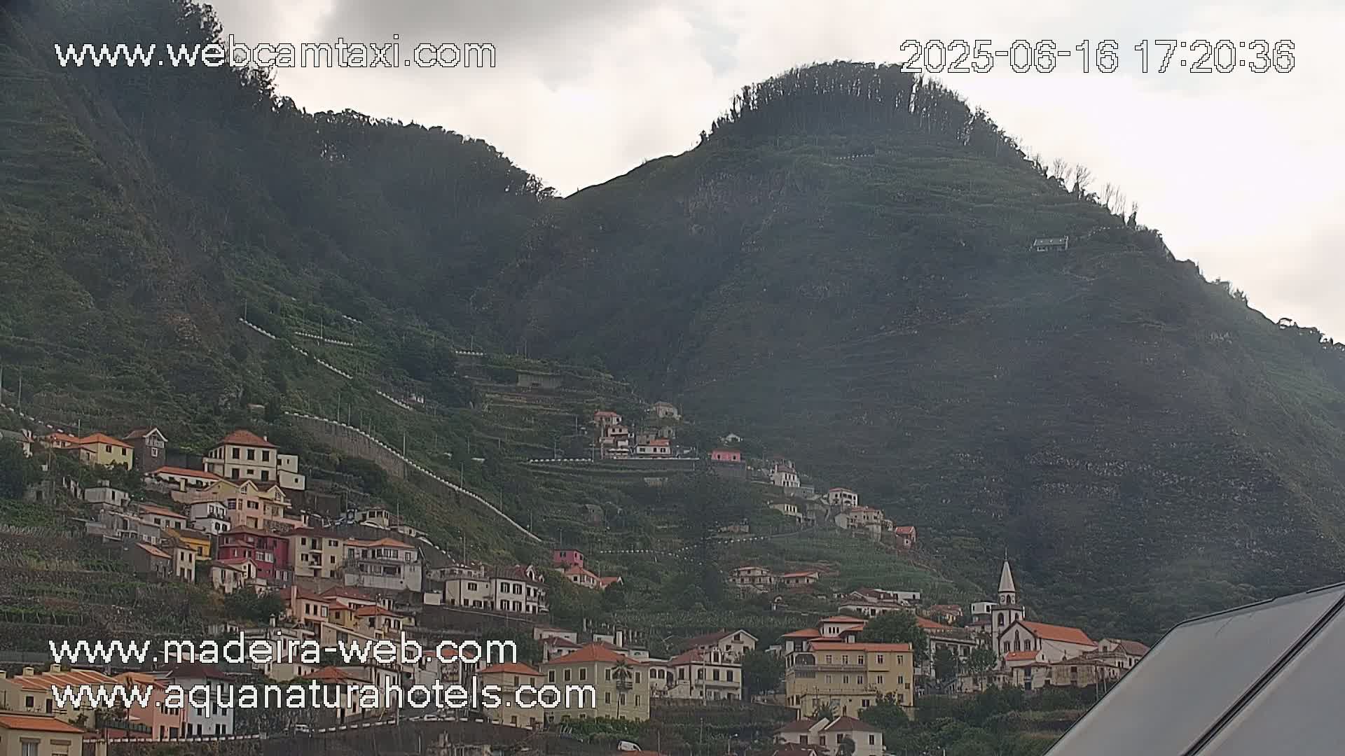 A village of colorful houses climbs a steep, terraced hillside under an overcast sky.