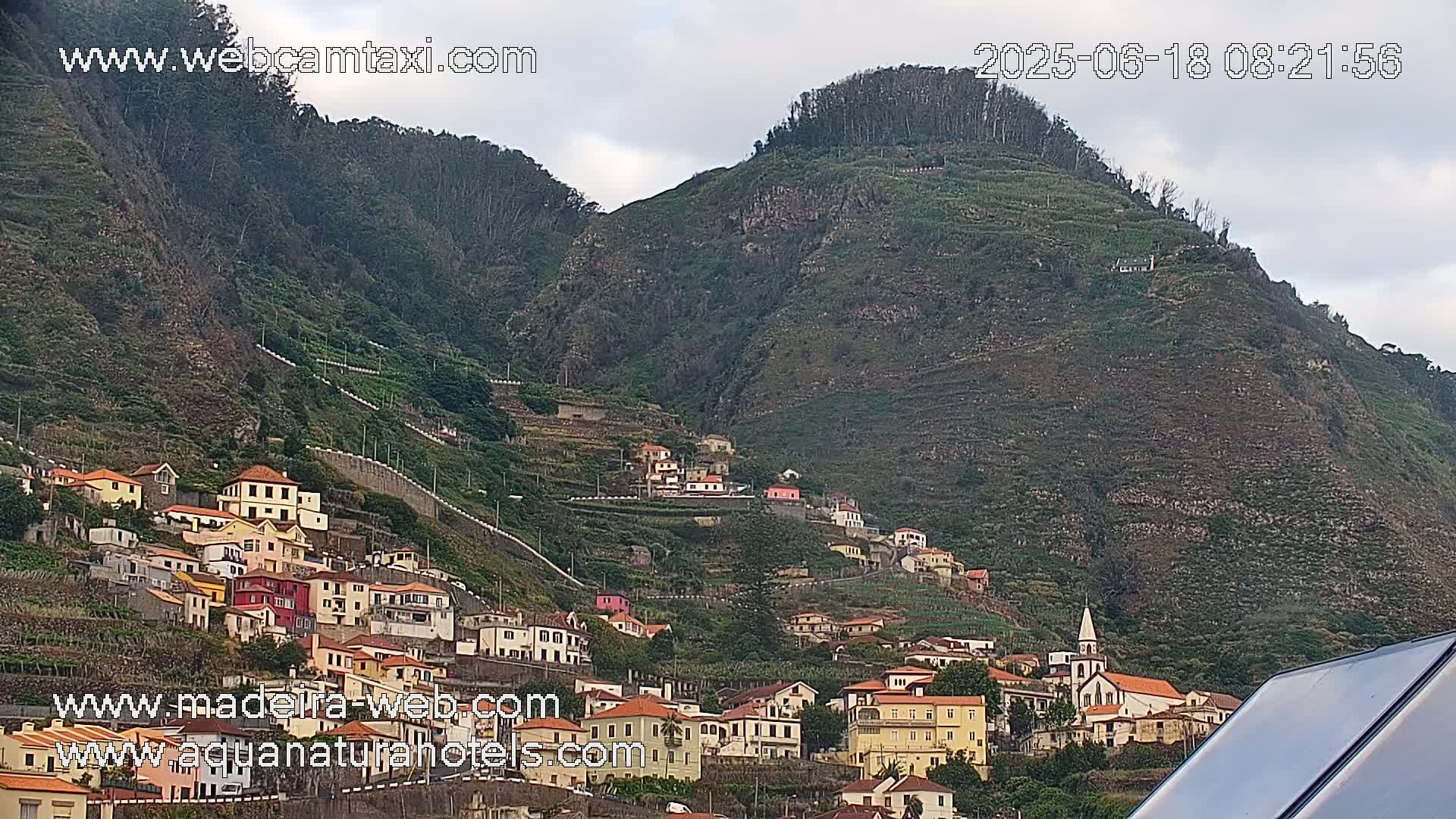 A hillside village with colorful houses clings to a steep, terraced mountainside under a cloudy sky.
