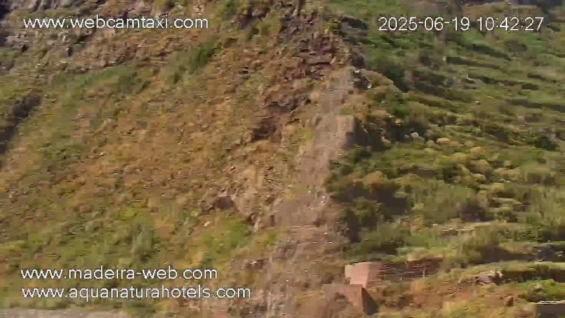 A rocky, scrub-covered hillside slopes downward, with a partially visible structure at the bottom.