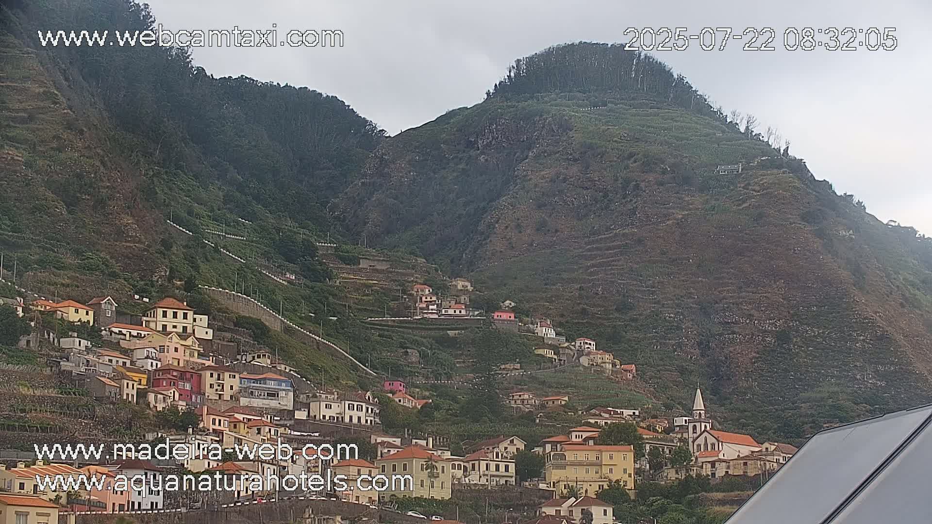 A hillside village of colorful buildings clings to a steep, terraced mountainside under an overcast sky.