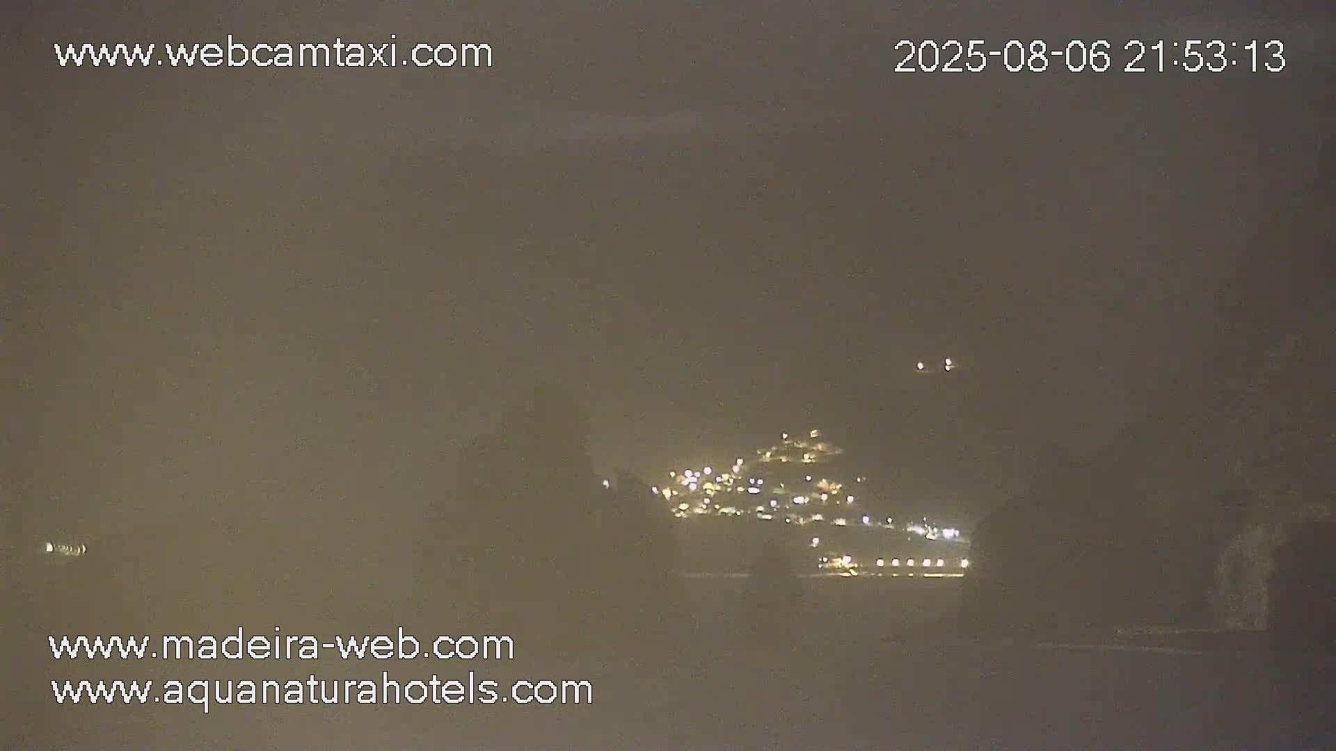 A hazy night scene shows a hillside town with illuminated buildings in the distance.