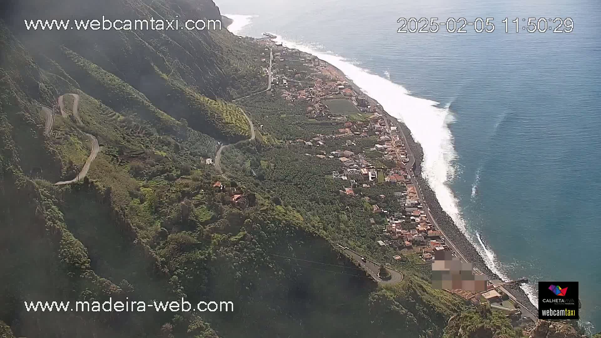 A coastal town nestled on a hillside overlooking a dark blue ocean with white-capped waves on a sunny day.