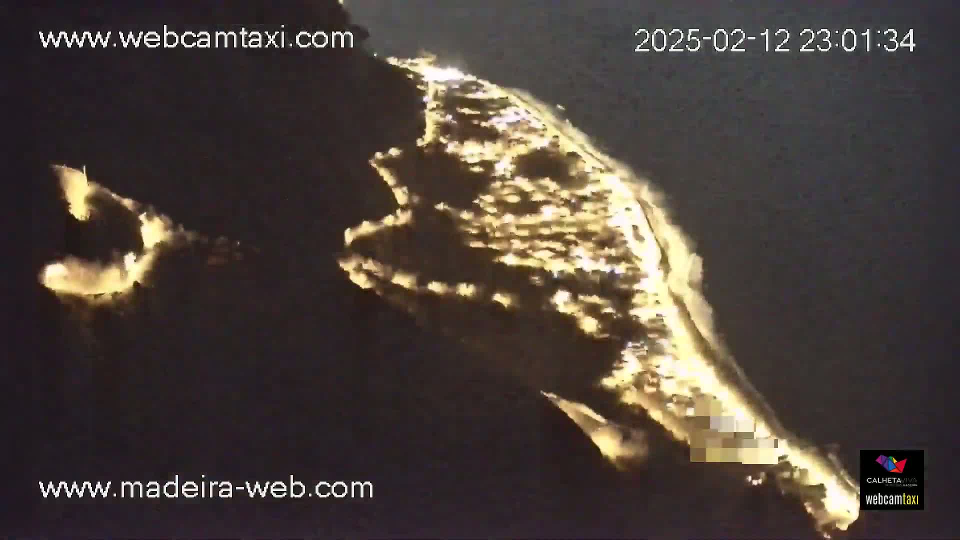 A nighttime, aerial view shows a coastline with lights illuminating a section of land and beach.