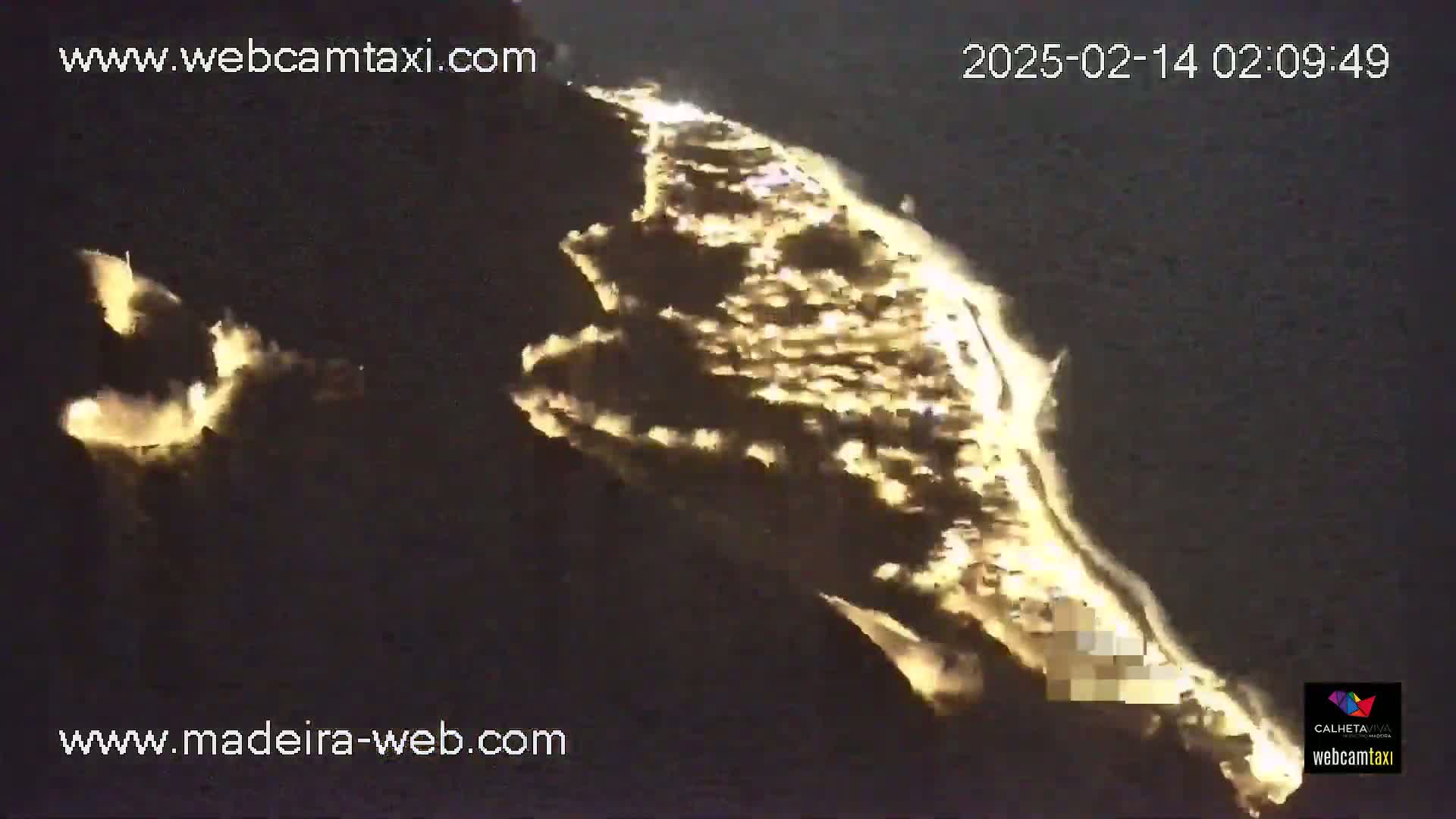 A long, narrow, brightly lit landmass, possibly a peninsula or island, is visible at night from an elevated vantage point.