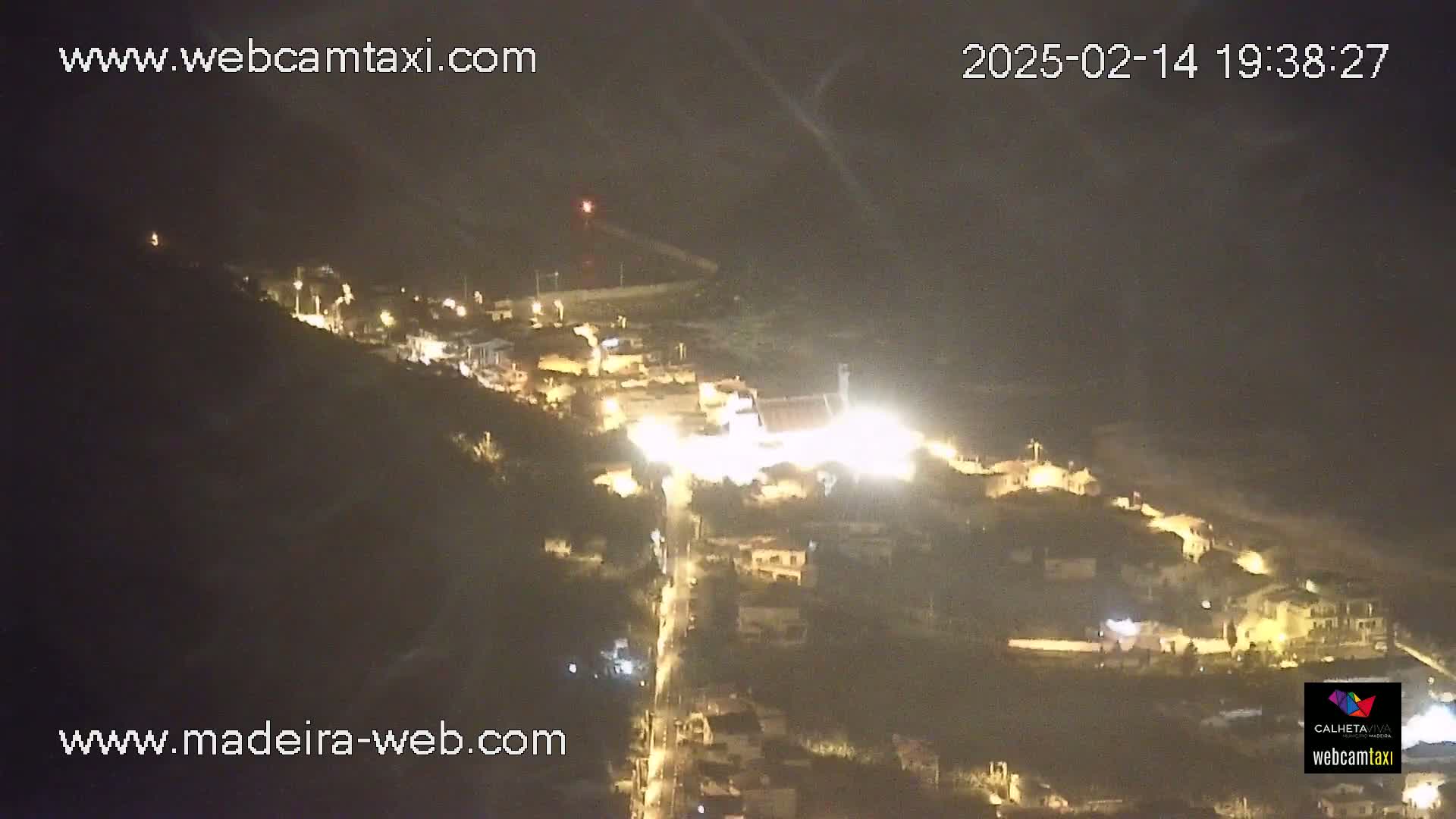 A nighttime, high-angle view shows a small town illuminated, nestled on a hillside.