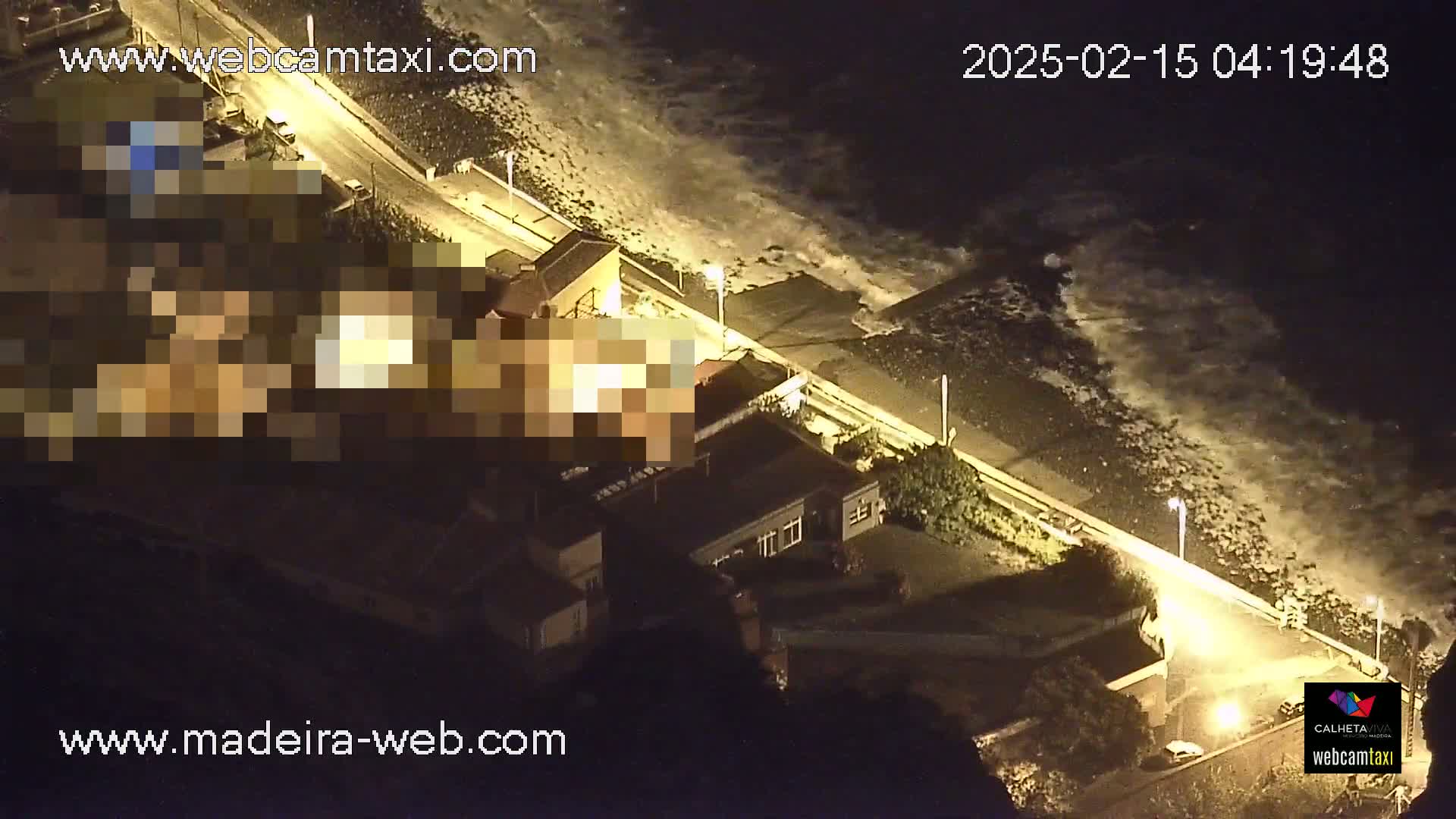 A nighttime aerial view shows a coastal road with buildings and large waves crashing on a dark beach.