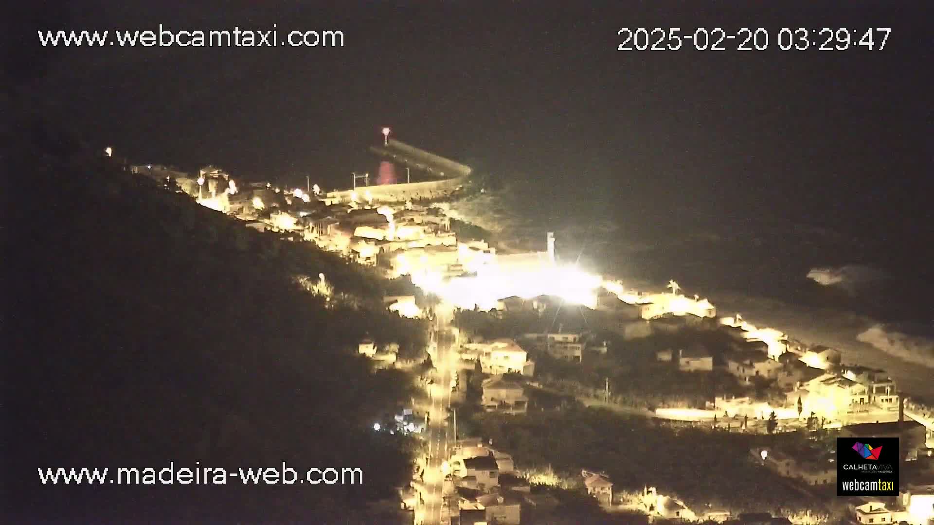 A nighttime, aerial view of a coastal town illuminated by streetlights, with dark, wavy water visible below.