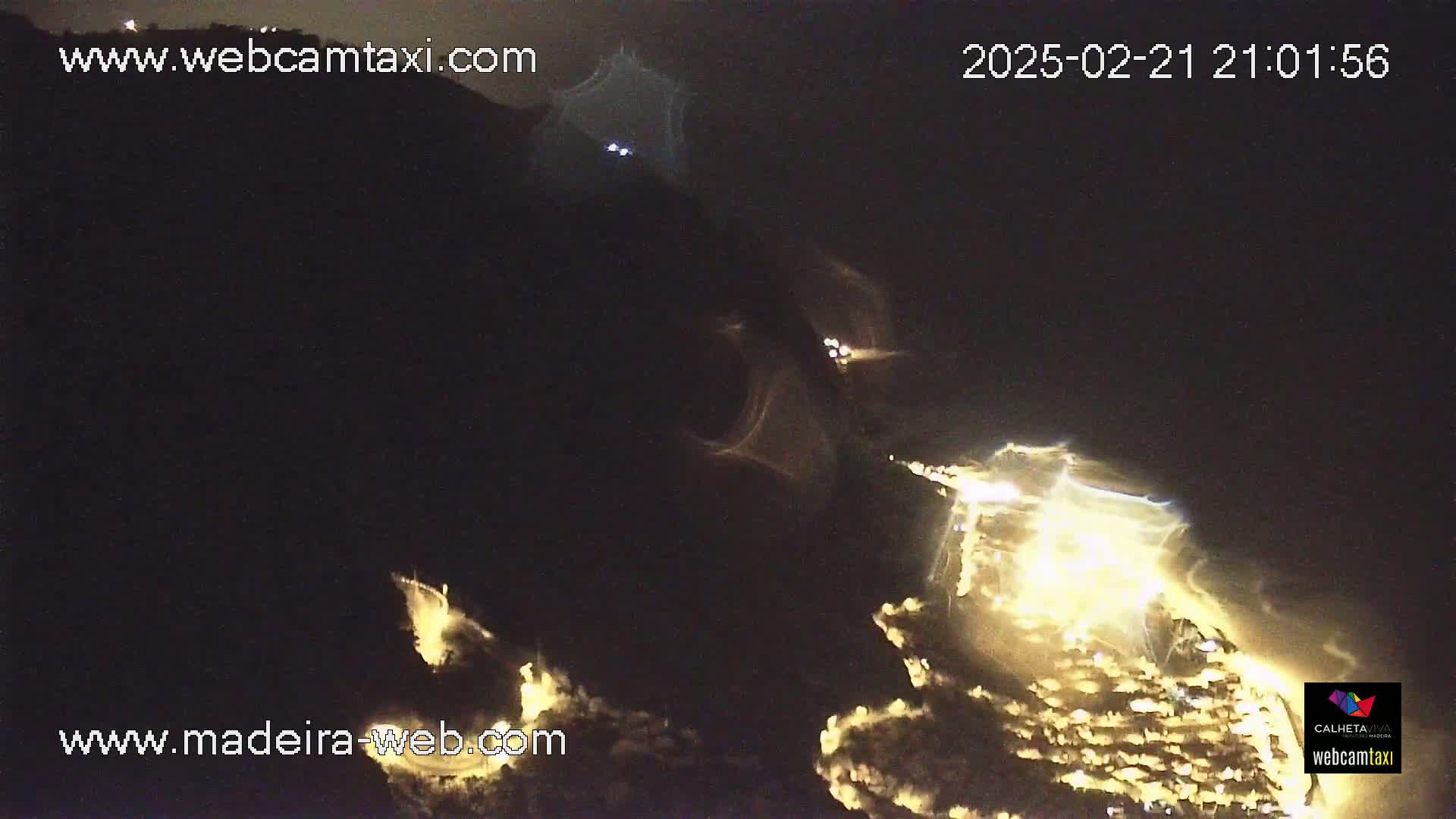 A nighttime, long-range view shows a town illuminated by lights nestled in a dark, mountainous area.