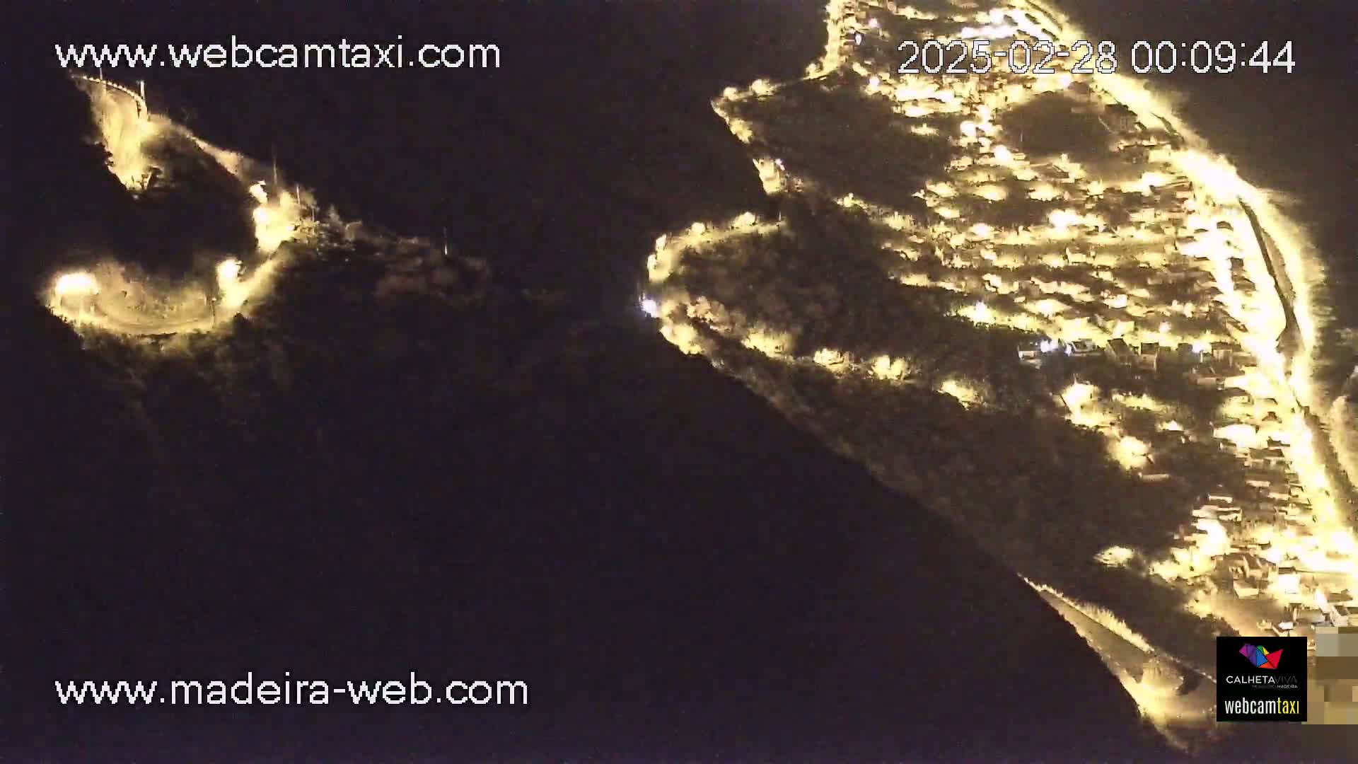 A nighttime aerial view shows two hillside settlements illuminated by numerous lights.