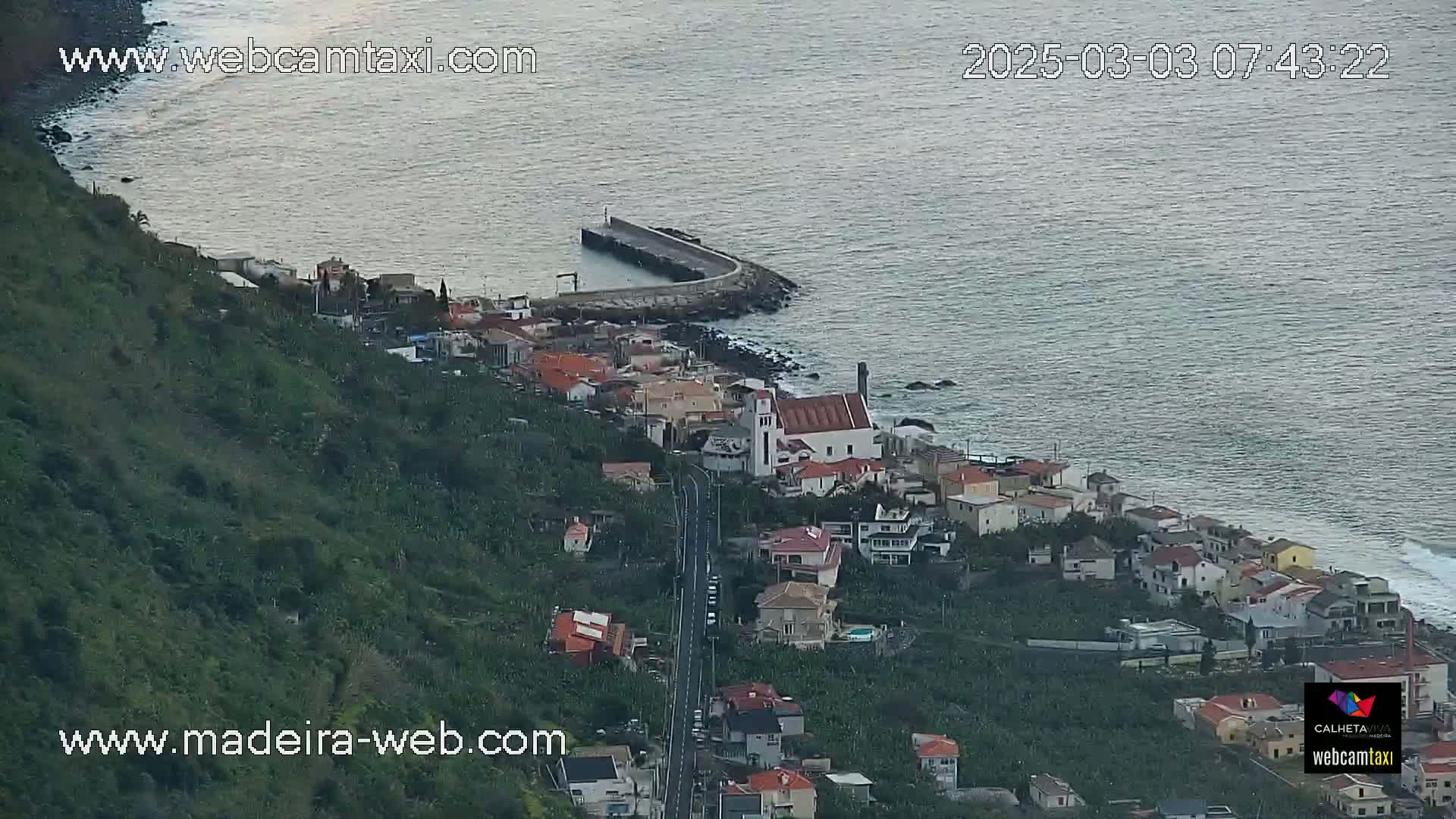 A coastal town with a church and a small harbor is nestled on a hillside overlooking a calm ocean.