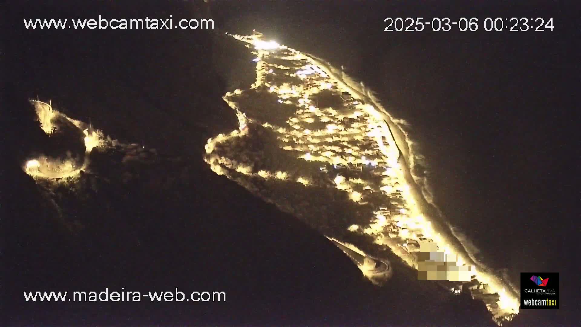 An aerial nighttime view shows a coastal town illuminated, with a dark ocean visible along the shoreline.