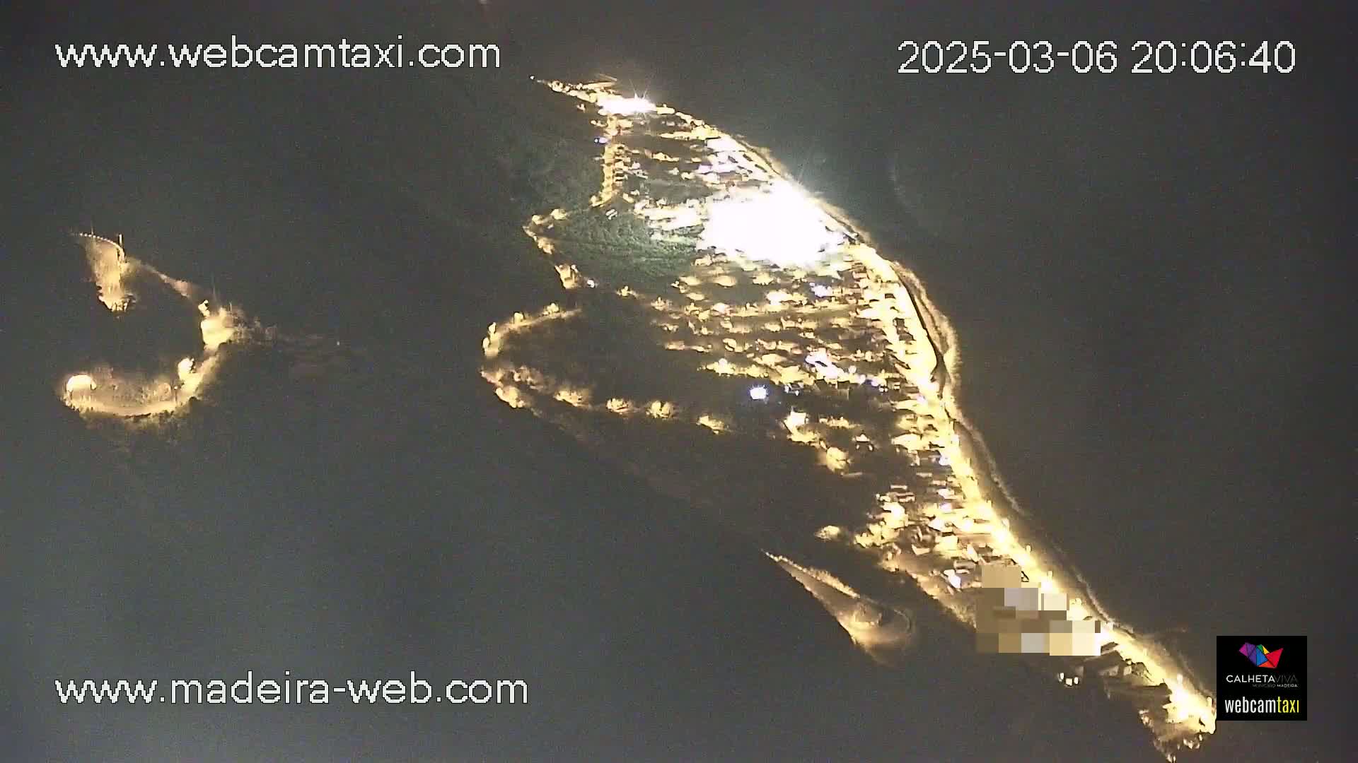 An aerial nighttime view shows a coastal town illuminated with numerous lights, under a clear, dark sky.