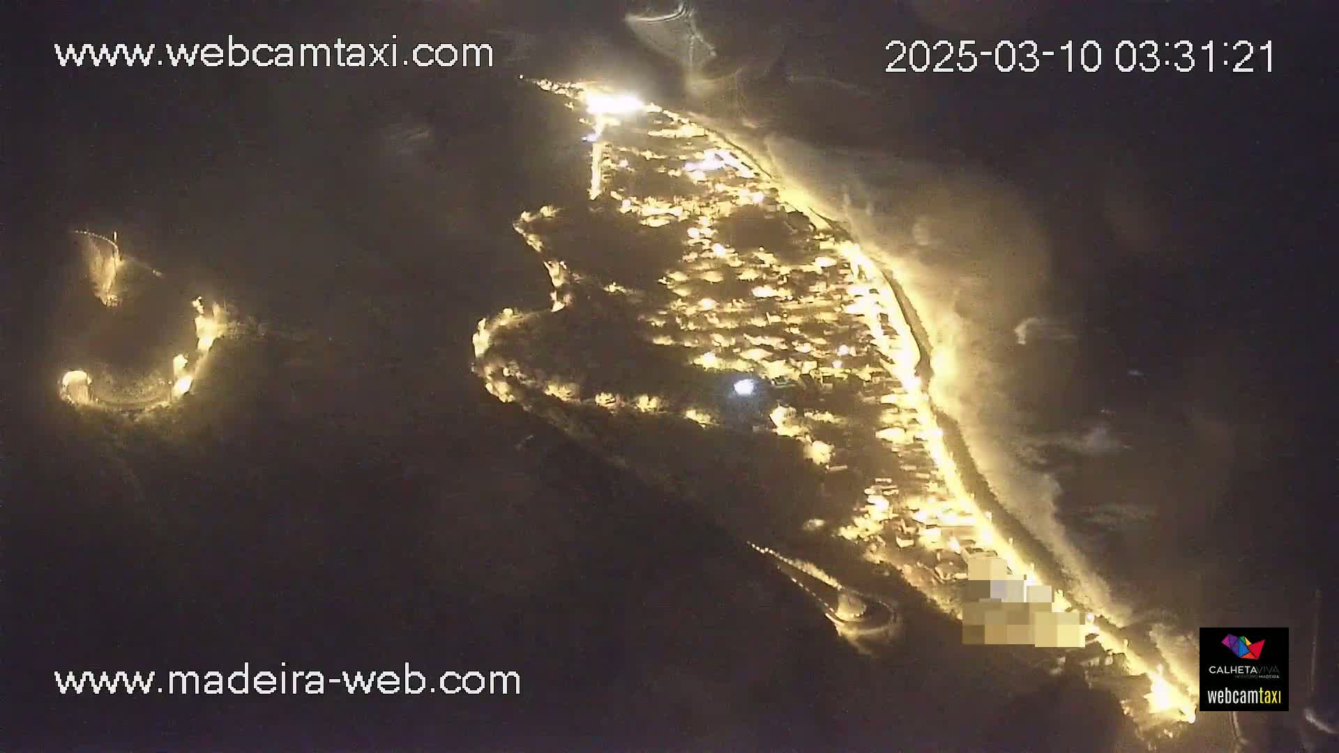 An aerial nighttime view shows a coastal town illuminated, with dark water visible along the shoreline.
