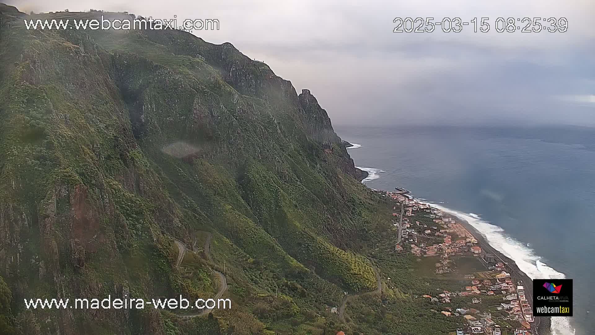 A steep, green cliff overlooking a coastal town and dark-blue ocean under an overcast sky.