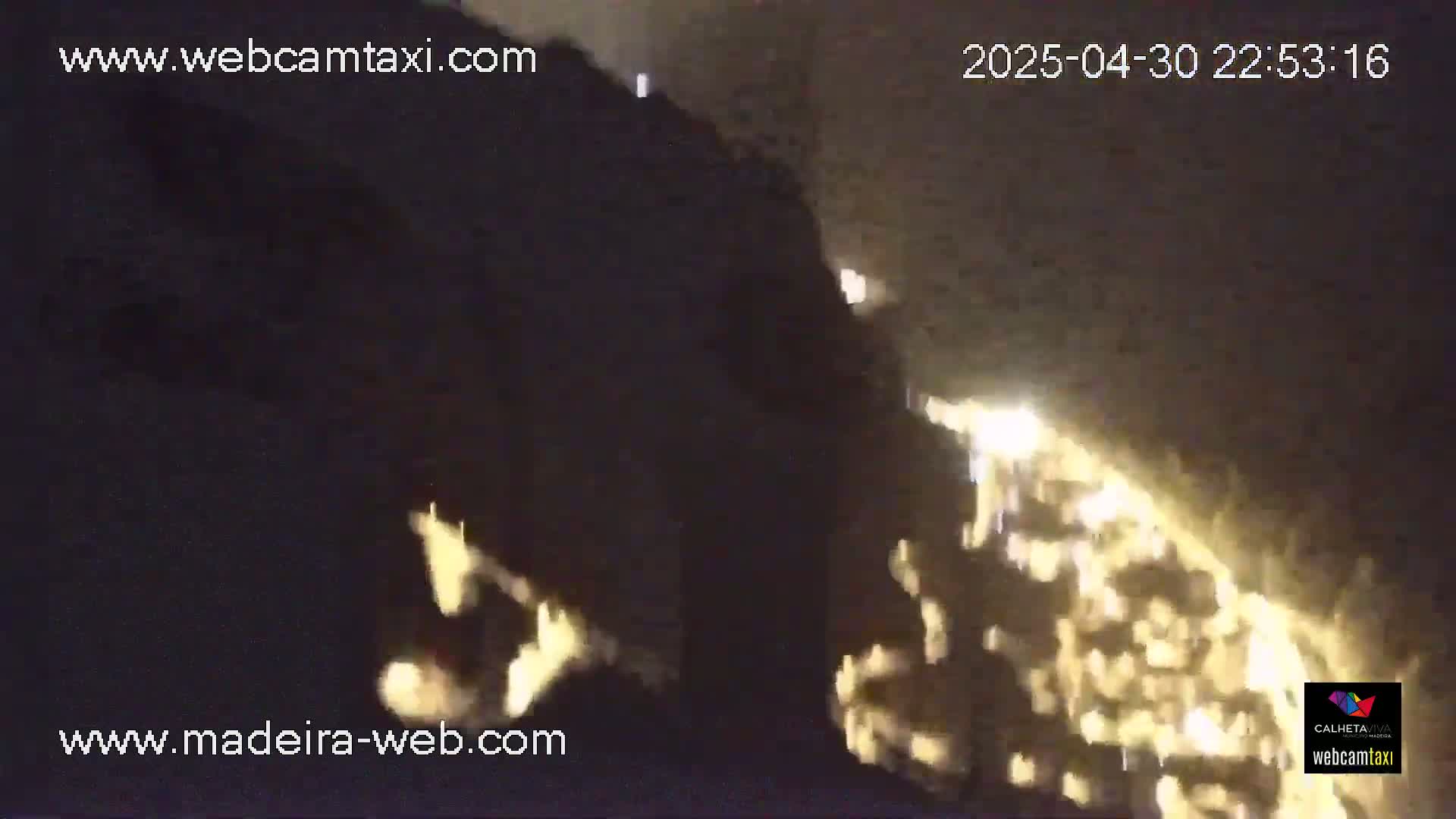 A nighttime, low-light image shows a brightly lit area, possibly a town or city, at the bottom of a dark, steep slope.