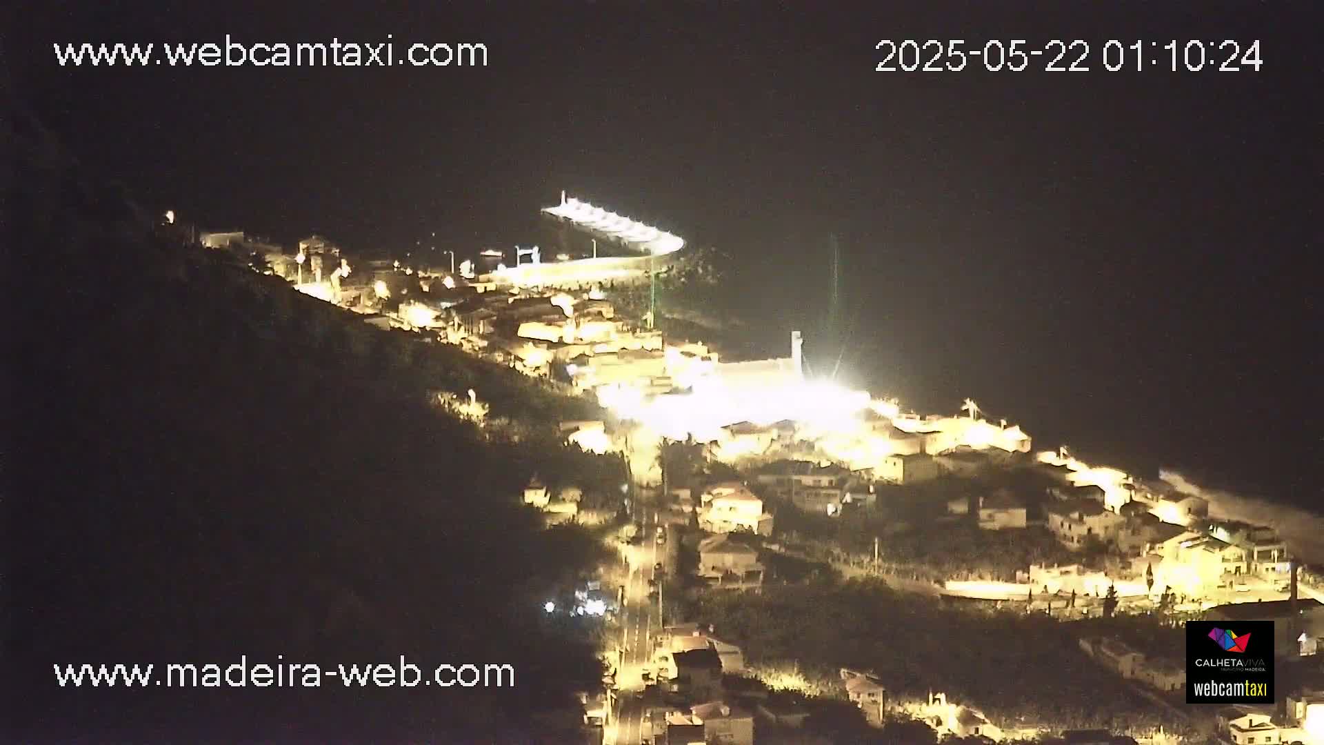 A nighttime, aerial view shows a small town illuminated on a hillside, under a clear, dark sky.