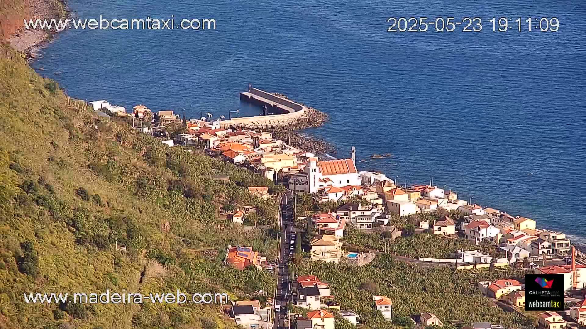 A coastal town with a church and a small harbor nestled on a hillside overlooking a calm, blue ocean.