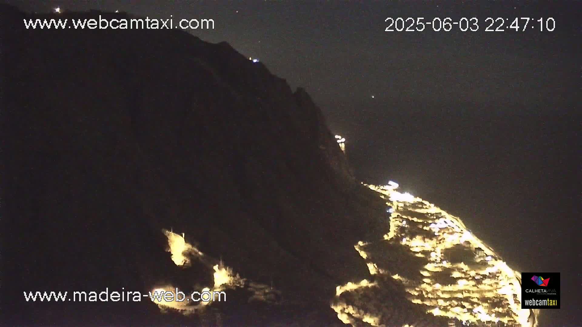 A nighttime view of a hillside town illuminated by lights under a clear, dark sky.