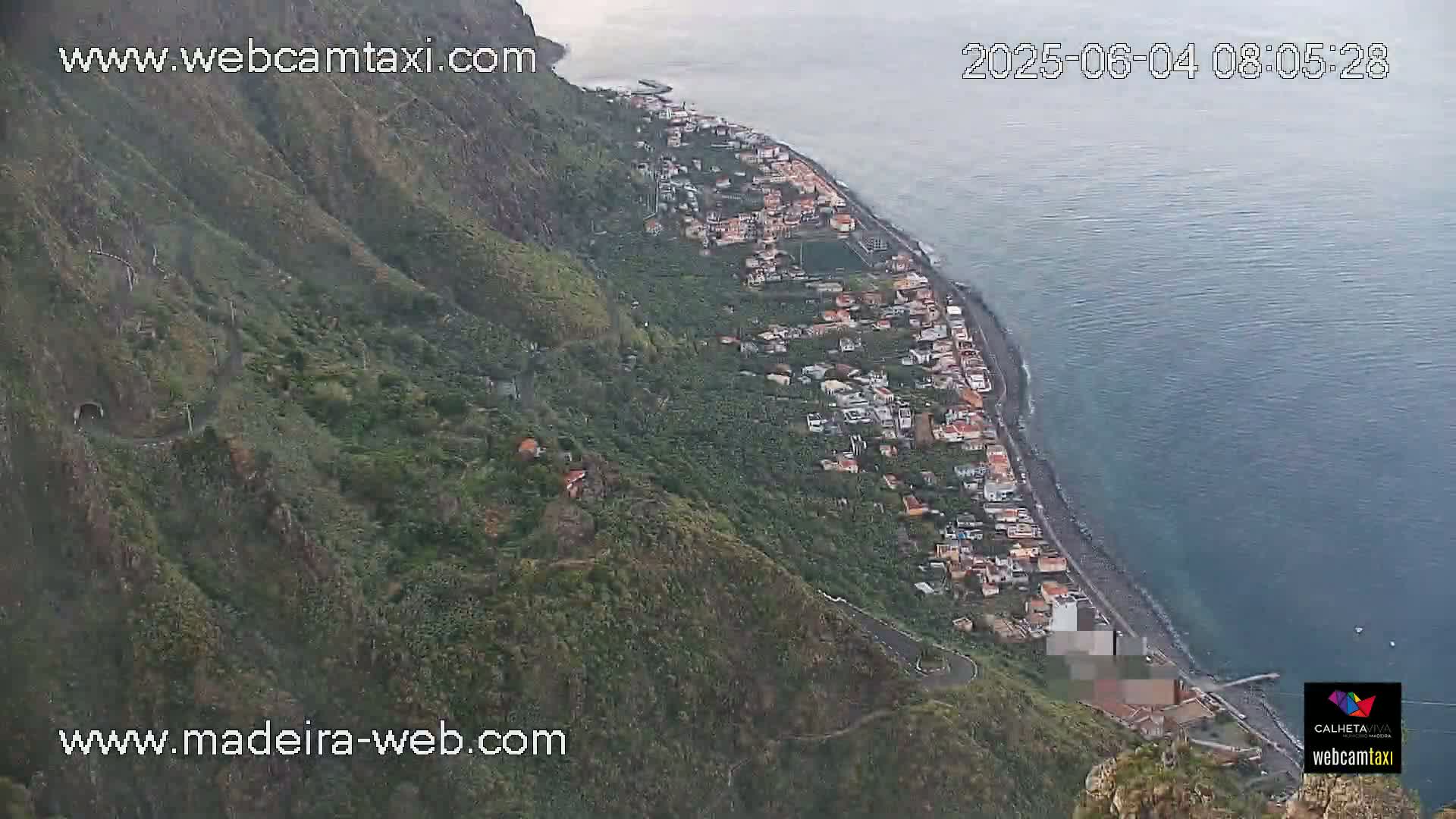 A coastal town nestled between a steep, green mountainside and a calm ocean.
