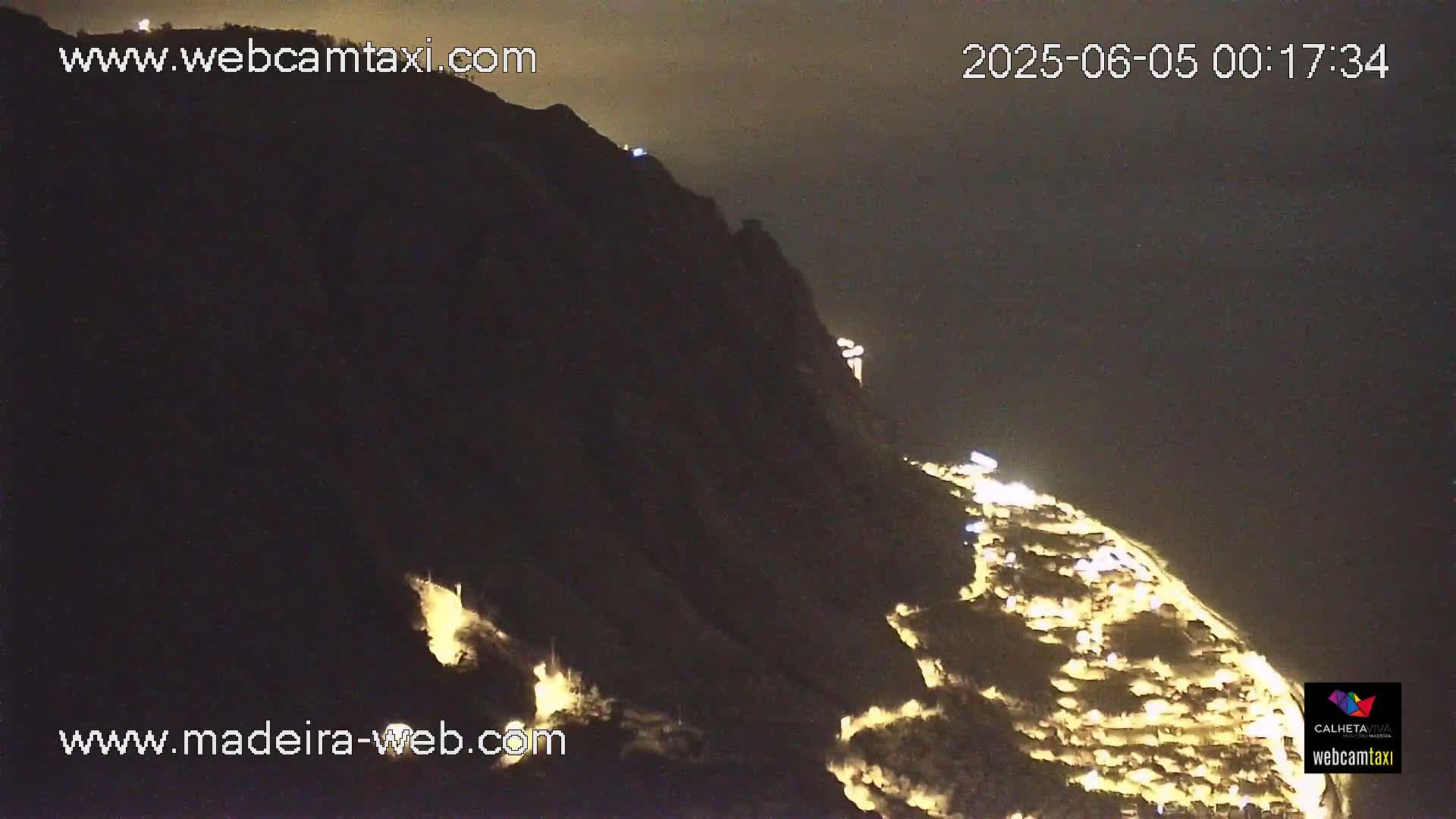 A nighttime view of a hillside town illuminated by lights, under a dark sky.