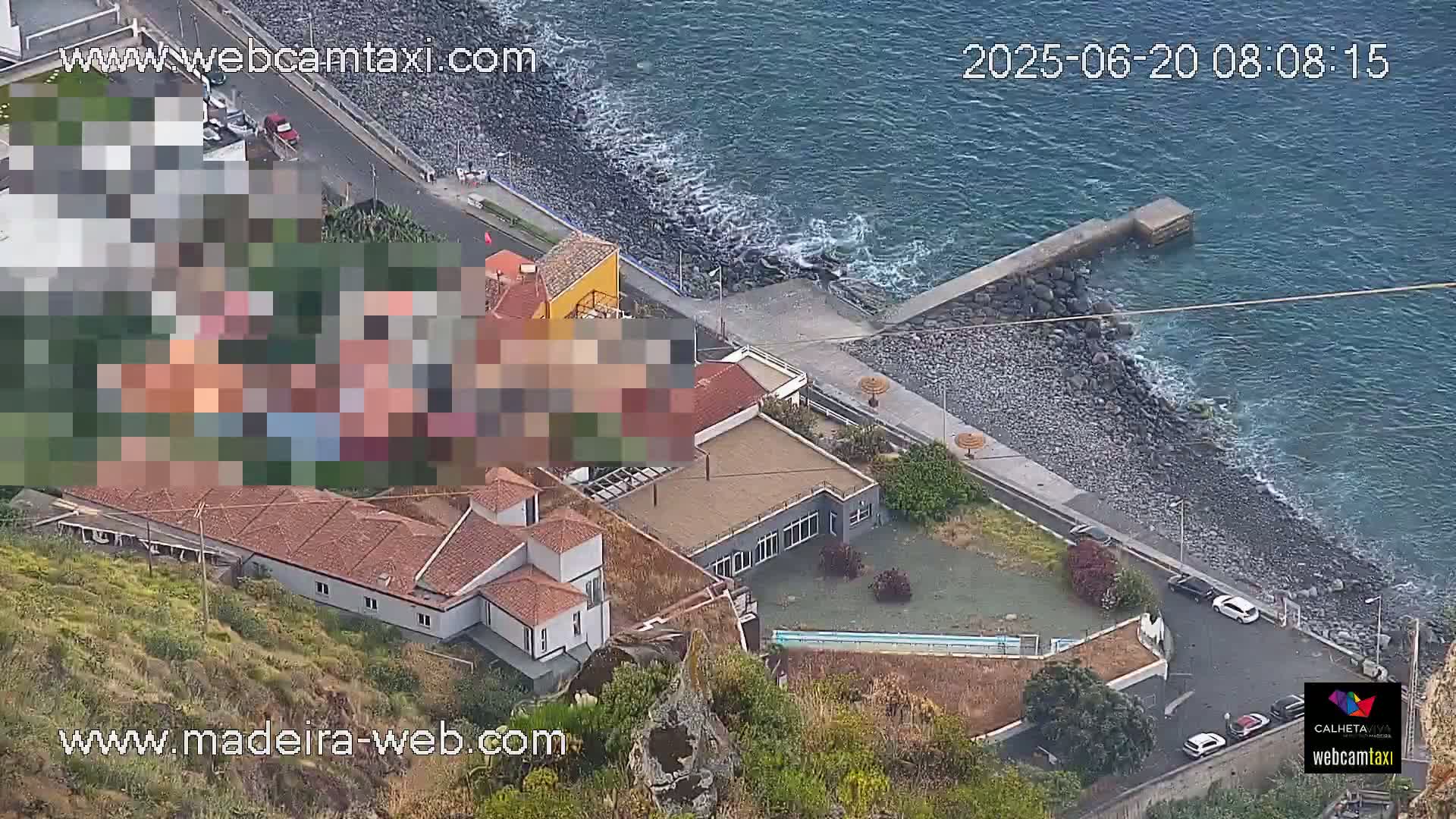An aerial view shows a coastal area with buildings, a rocky shore, and a calm ocean.