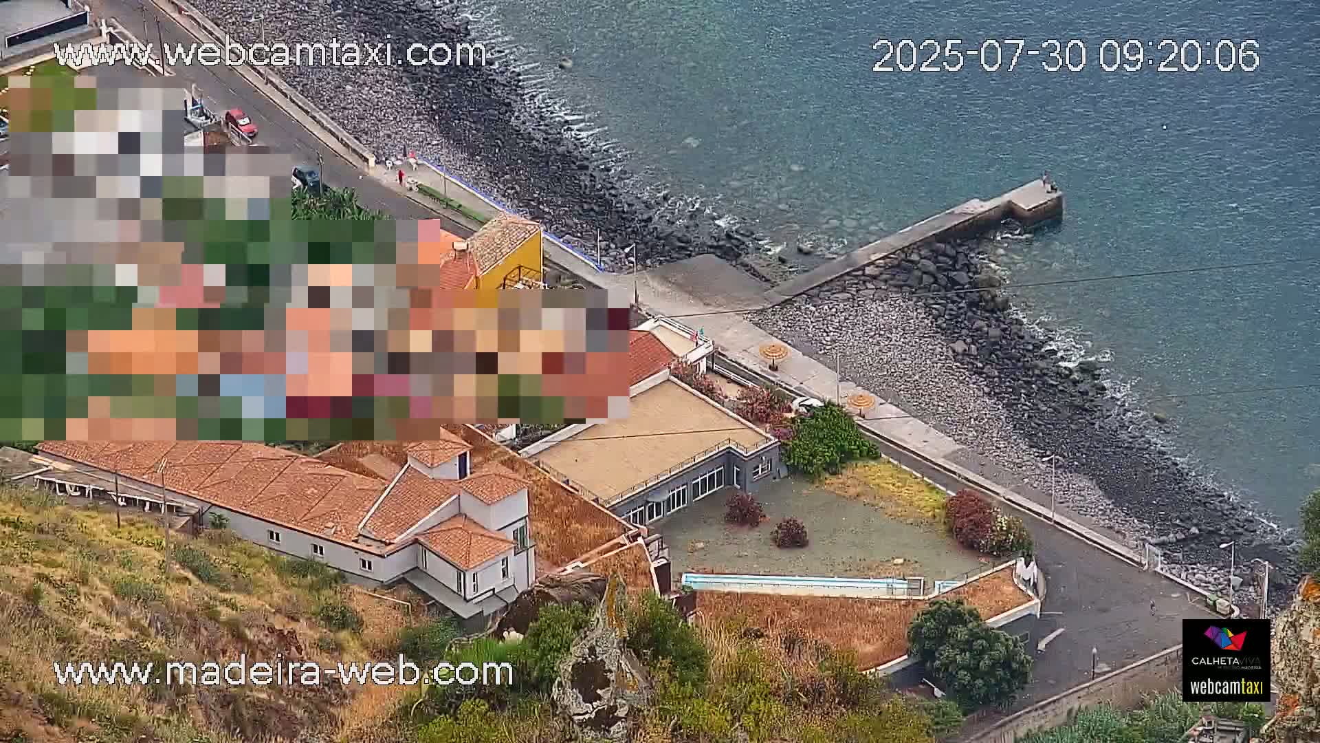 An aerial view shows a coastal area with a building complex, a rocky shoreline, and calm ocean water.