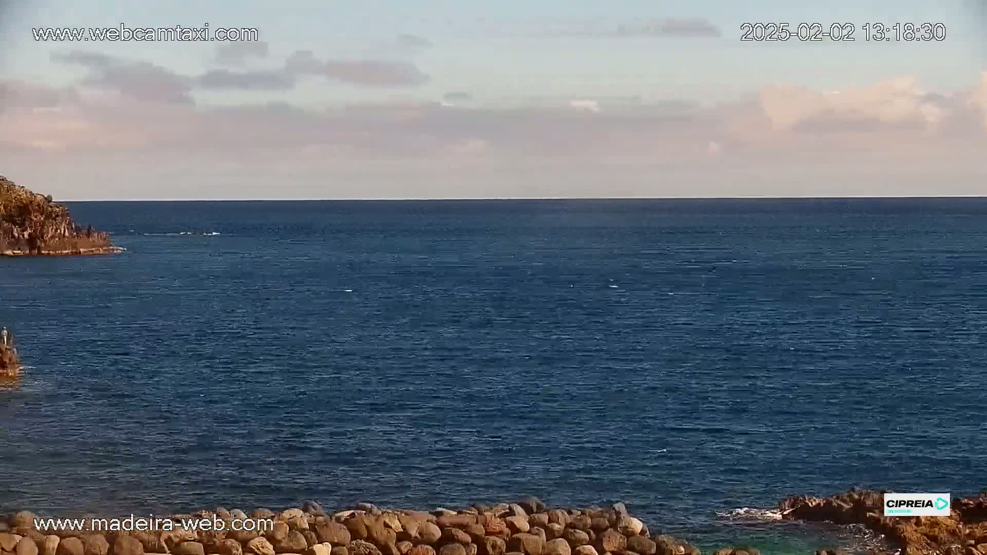 A mostly clear sky overlooks a dark blue ocean meeting a rocky shore.