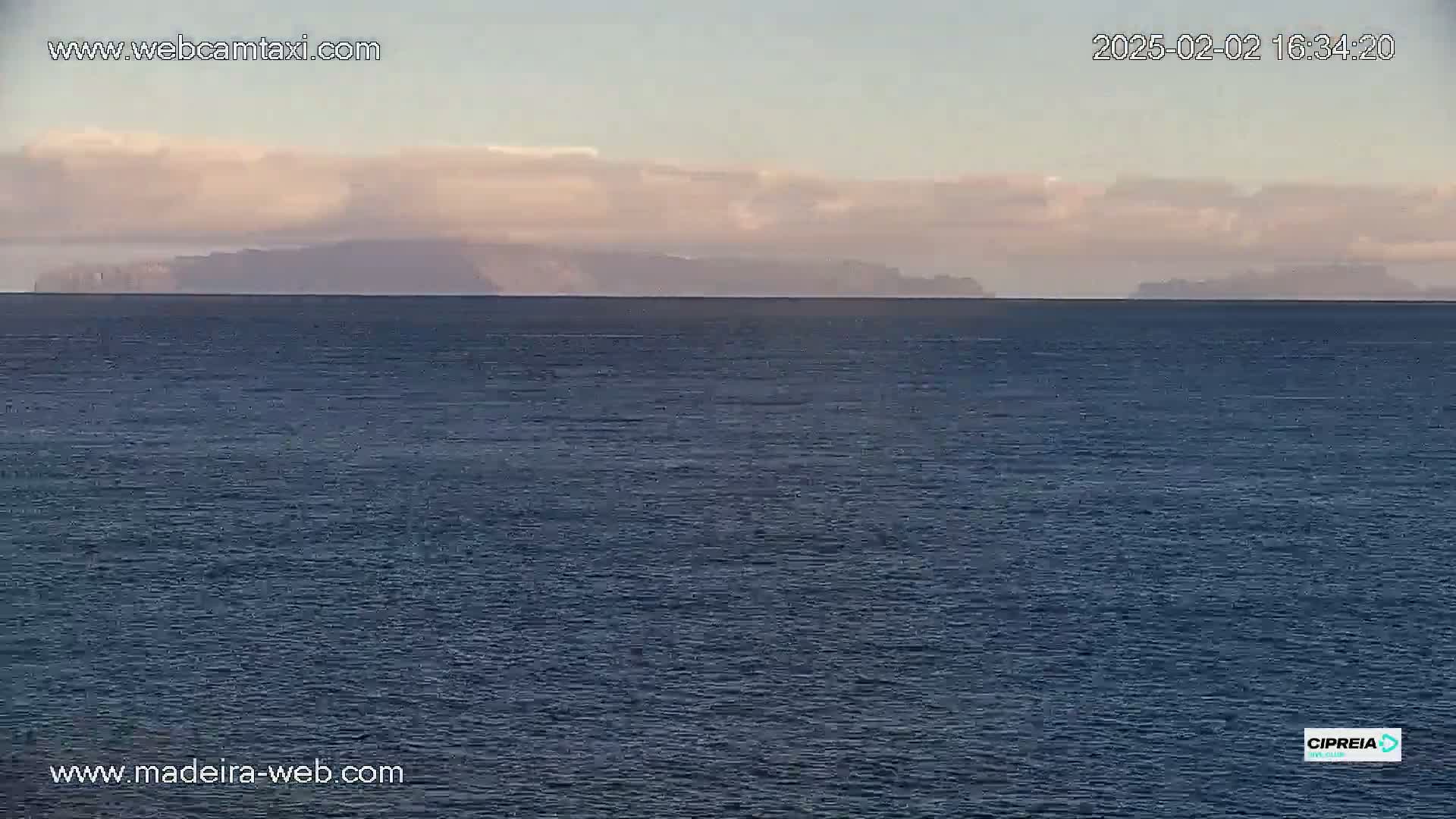 A calm, dark-blue ocean stretches to a distant line of mountains under a partly cloudy sky.