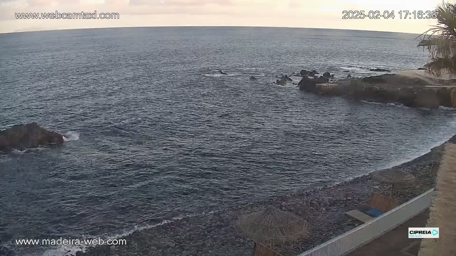 A rocky shoreline meets a dark, calm ocean under a partly cloudy sky.