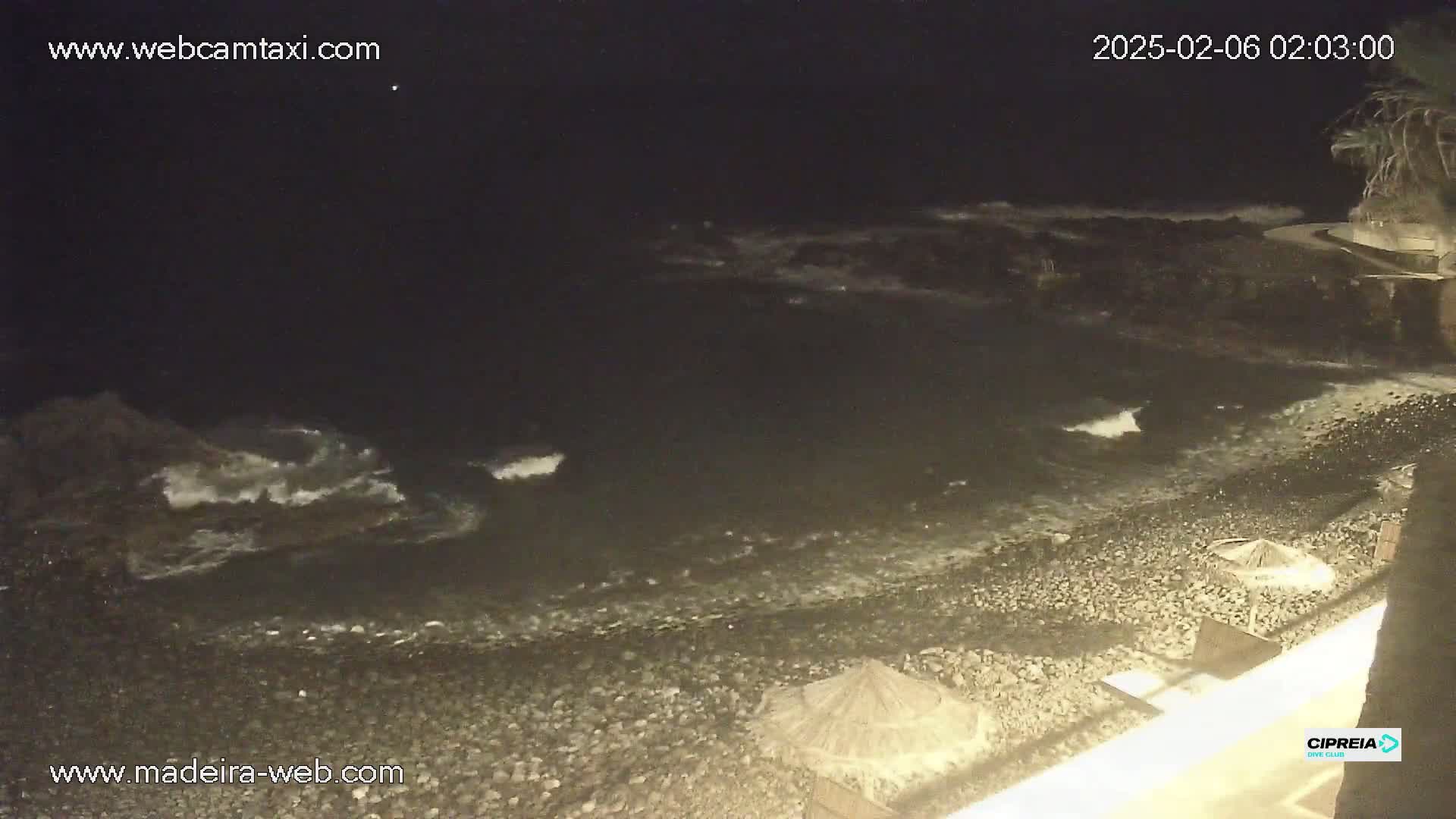 A dark, pebble beach is gently lapped by waves at night.