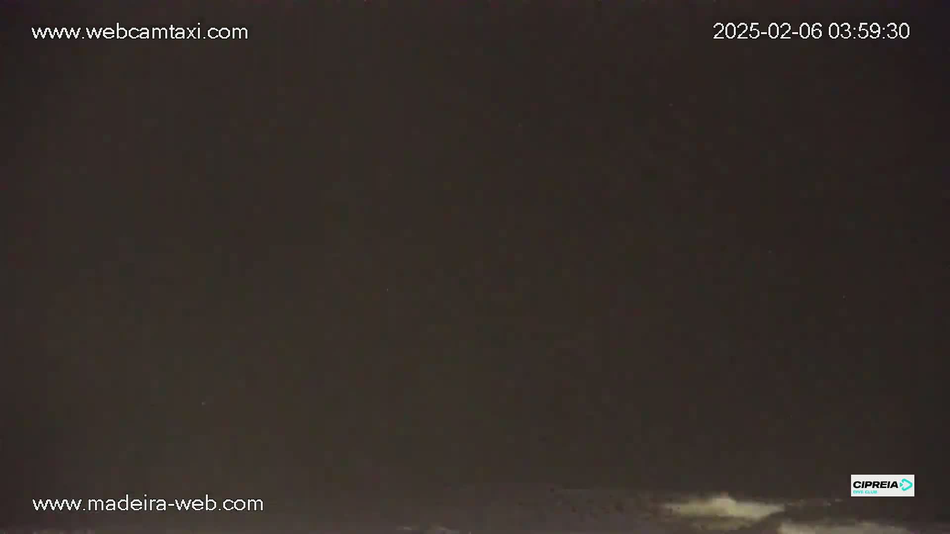 A dark nighttime scene shows a body of water with faint white waves at the bottom of the frame under a mostly clear, dark sky.