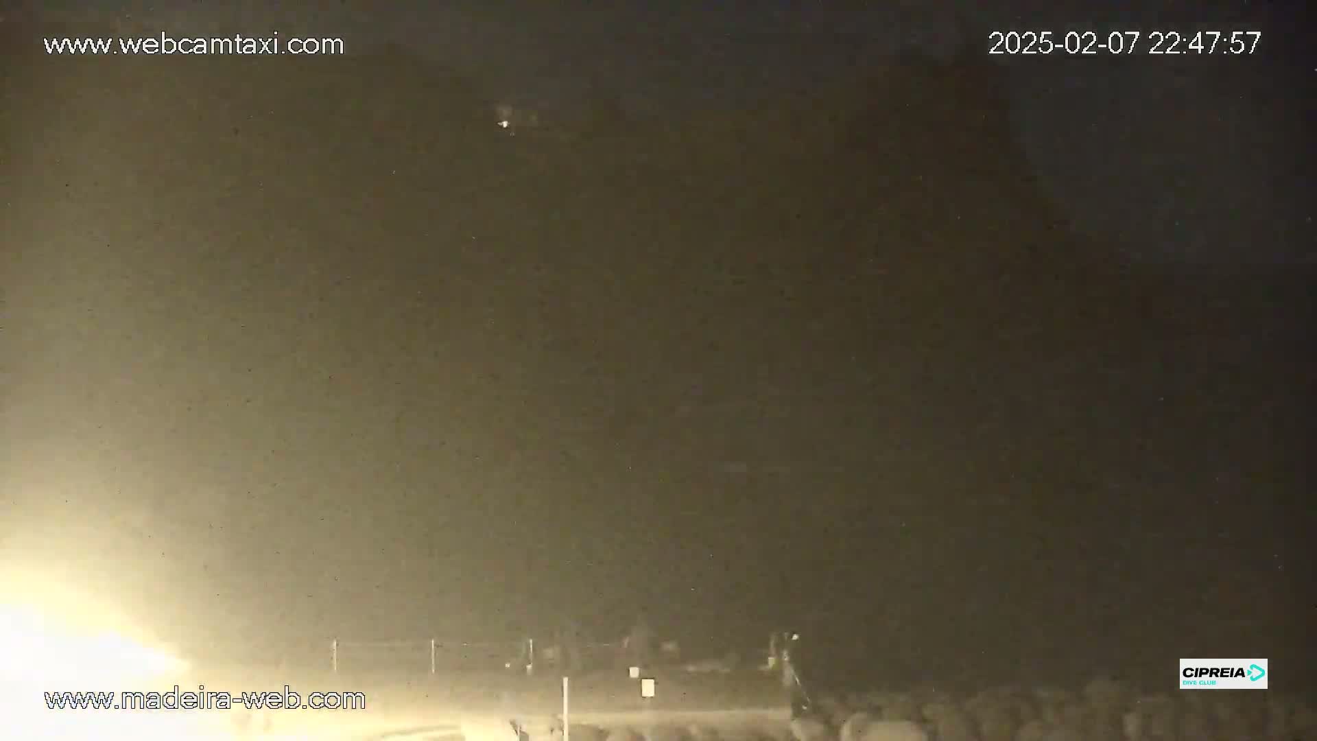 A nighttime, hazy scene shows a dark landscape with a faint light source in the lower left corner.