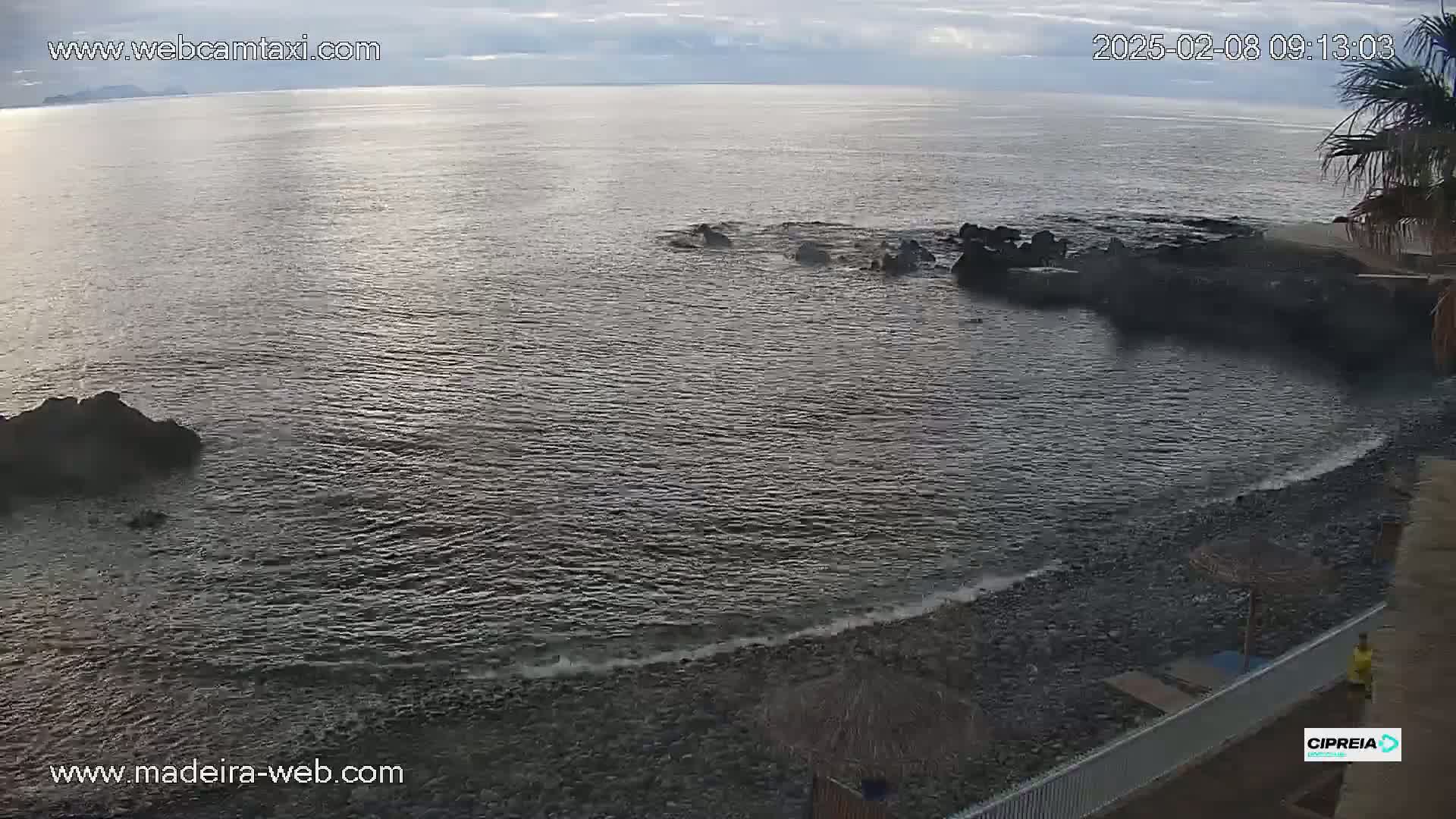 A rocky shoreline meets a calm, dark-grey ocean under a cloudy sky.