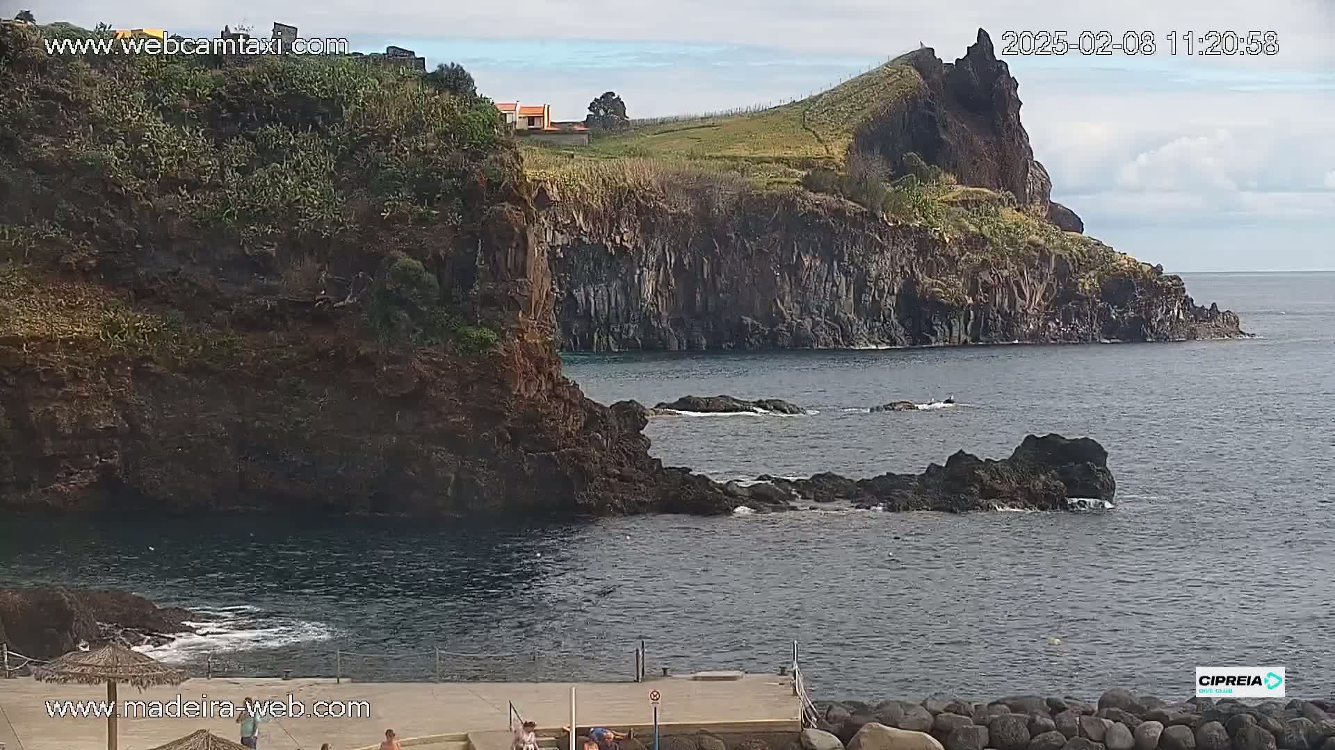 A rocky coastline with dark cliffs and a small, calm cove under partly cloudy skies.