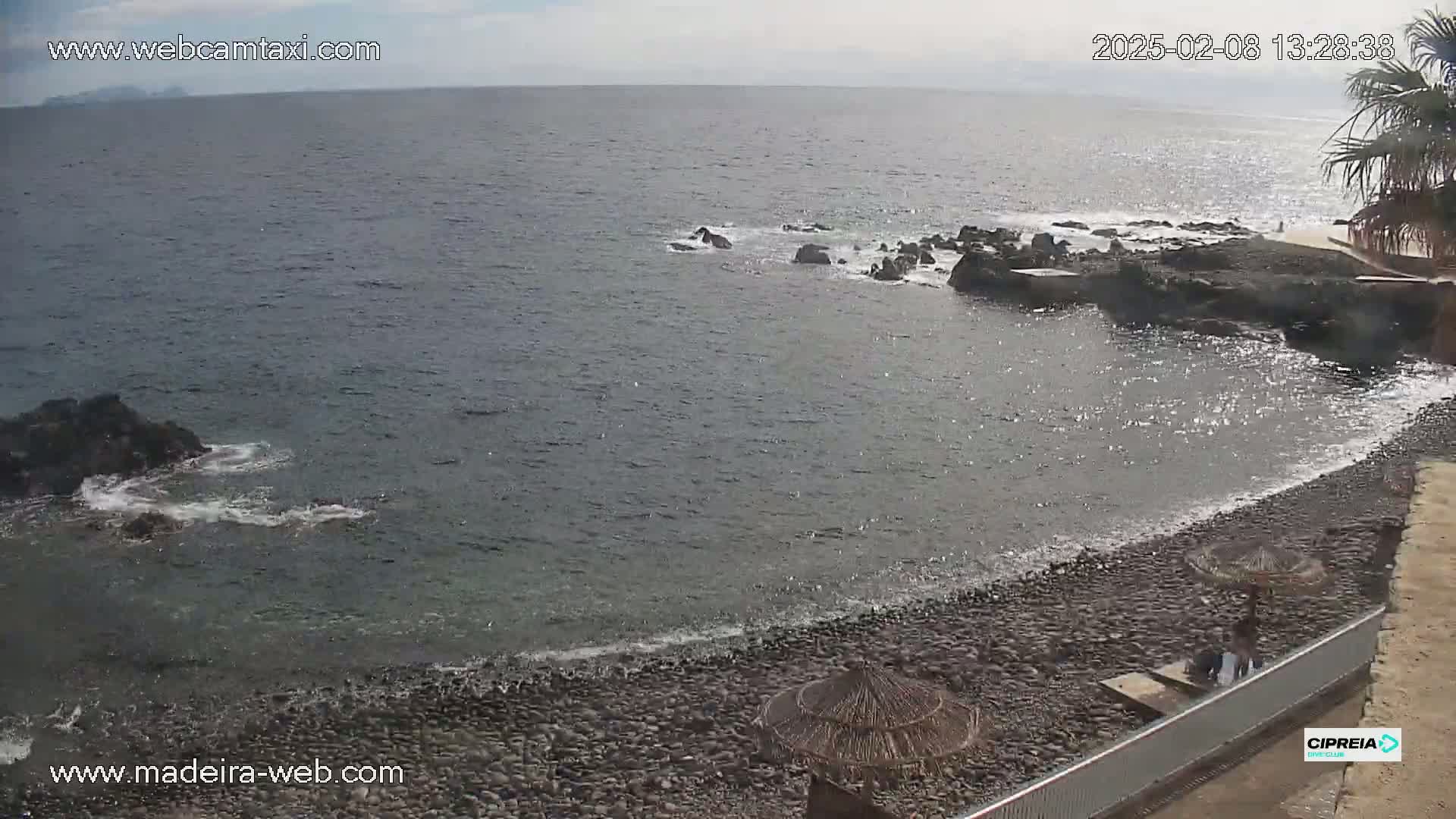 A rocky beach with calm ocean waves under a mostly cloudy sky.