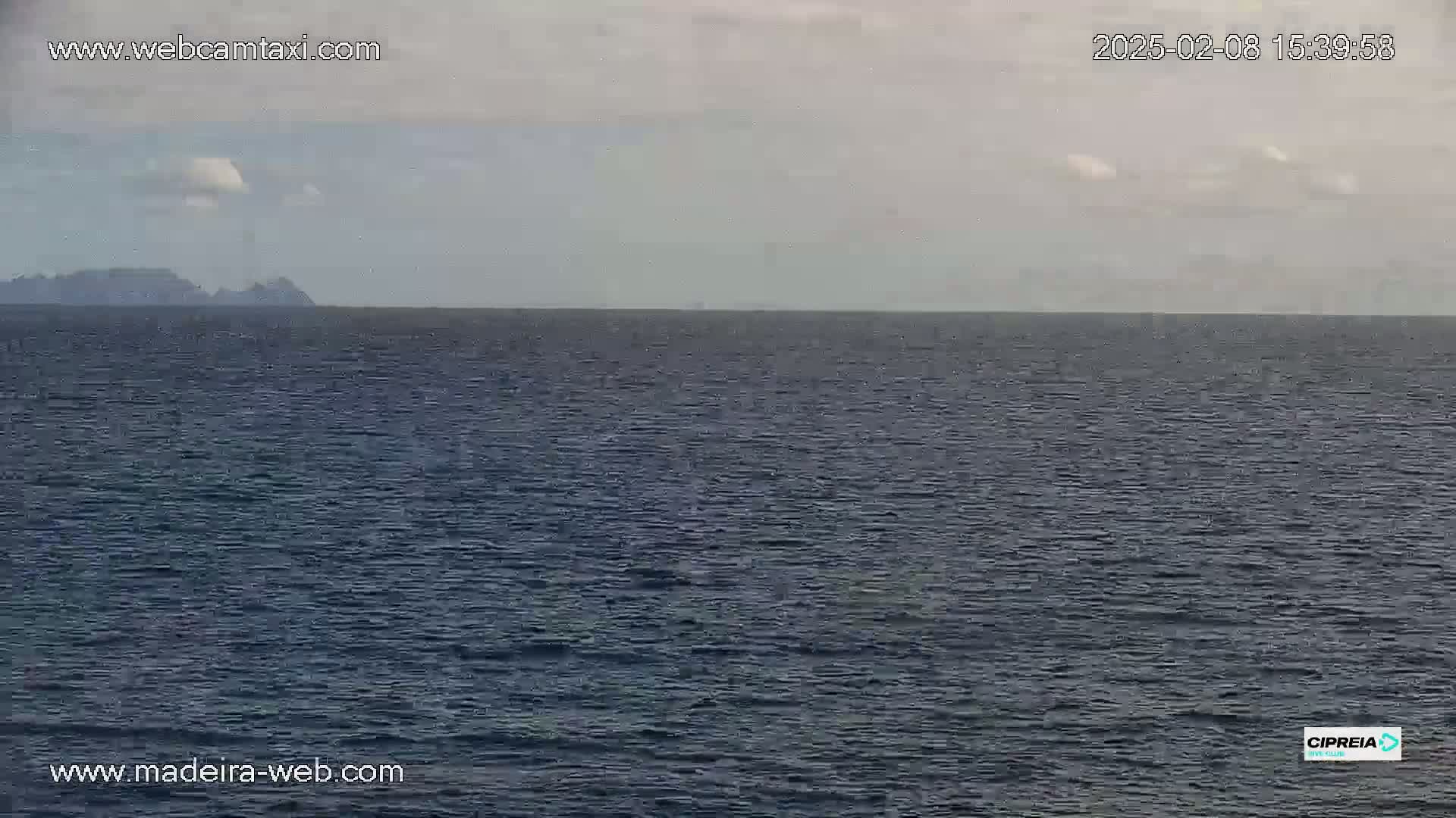 A calm, overcast day shows a dark blue ocean with a distant, low-lying landmass on the horizon.
