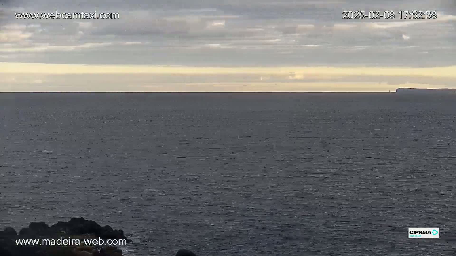 A dark-grey ocean stretches to a pale horizon under a mostly cloudy sky.